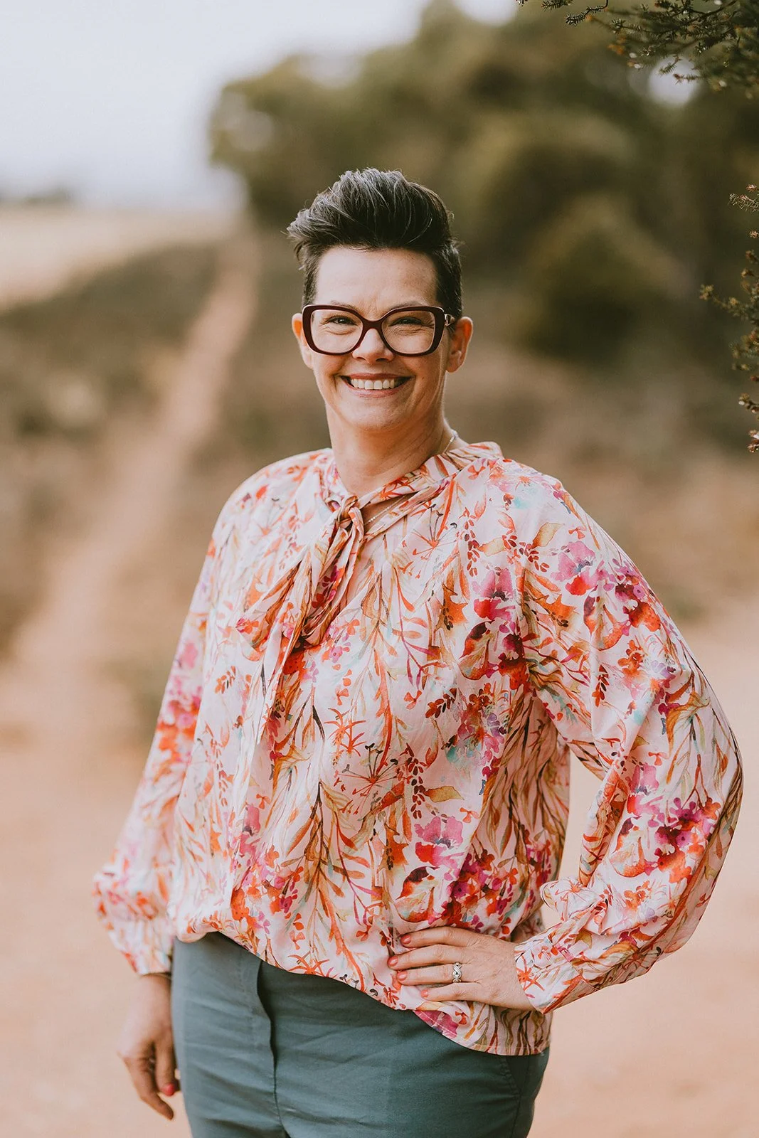 woman with short hair and wearing glassed standing with hand in hip on a dirt track next to a paddock in rural south australia