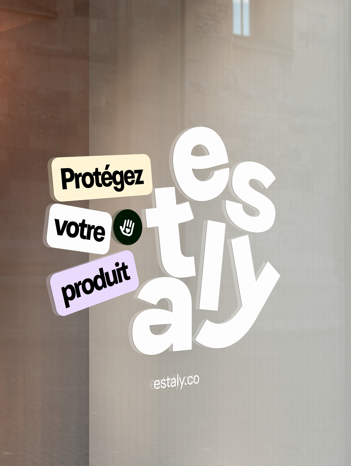Mot en lettres blanches indiquant 'é', 's', 't', 'a', 'l', 'y', '.', 'c', 'o', avec des messages en français 'Protégez votre produit' et un symbole d'arrêt ou de sécurité.