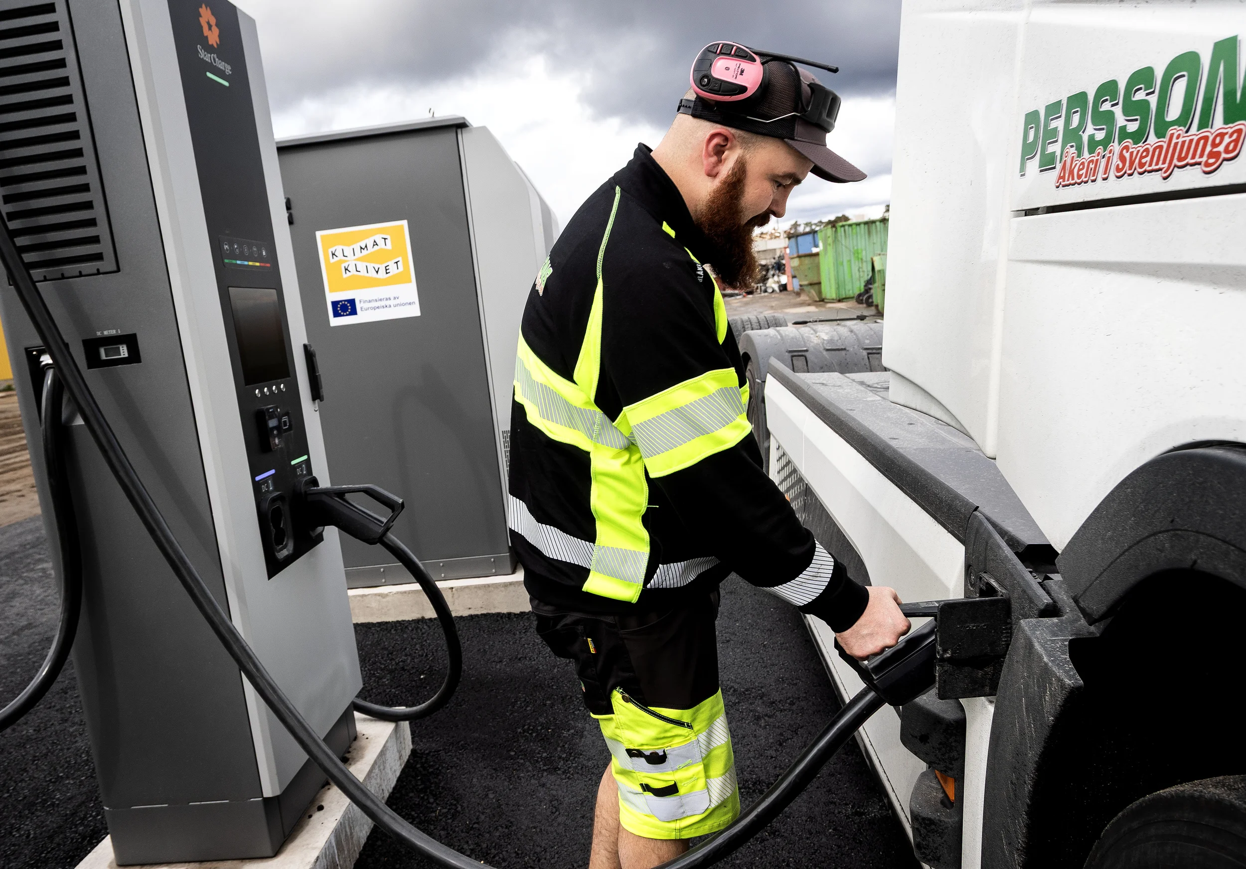 En man i en refleksväst laddar en elektrisk lastbil.