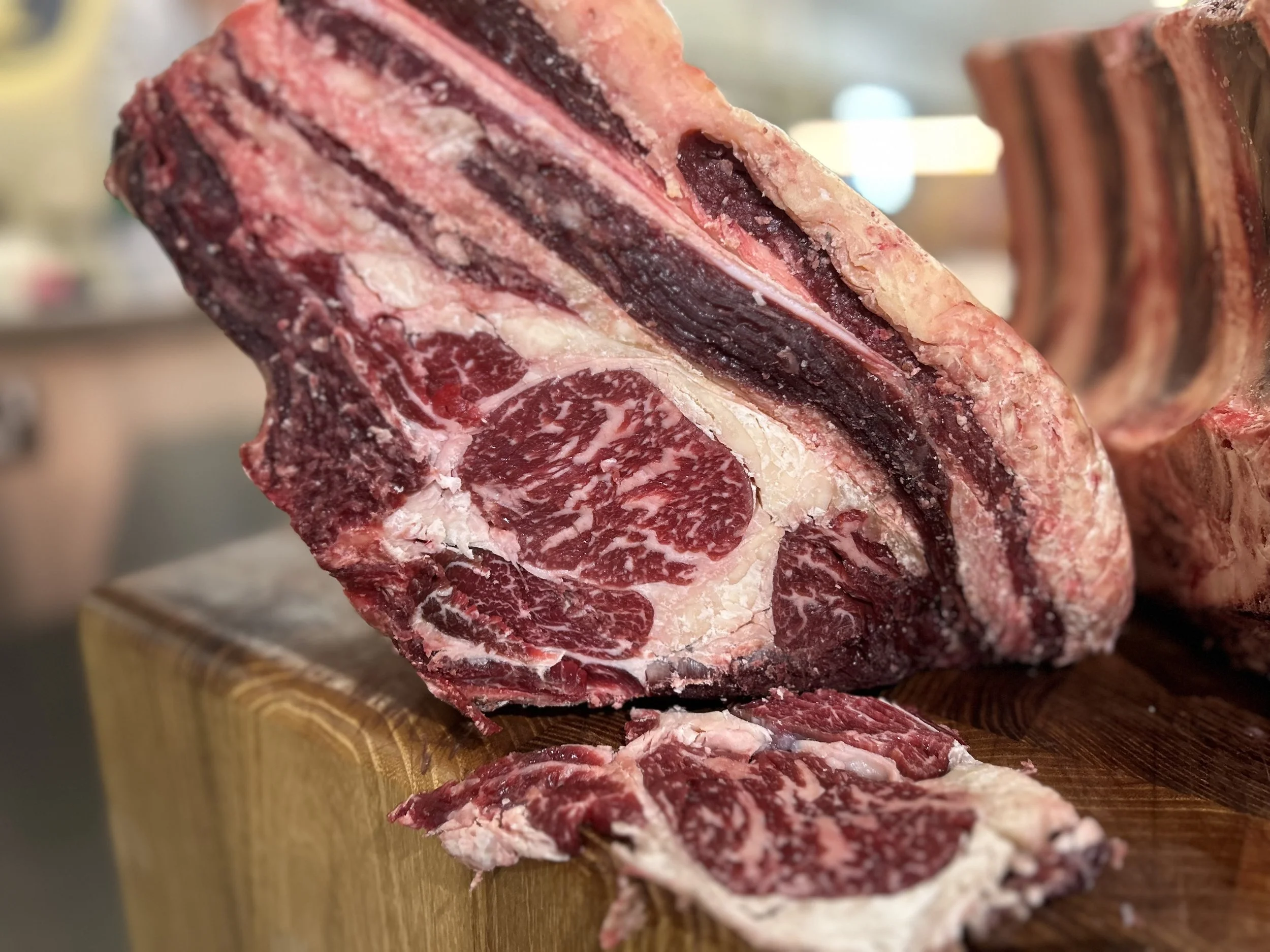 Large cut of marbled raw beef with visible fat and muscle, placed on a wooden cutting board.