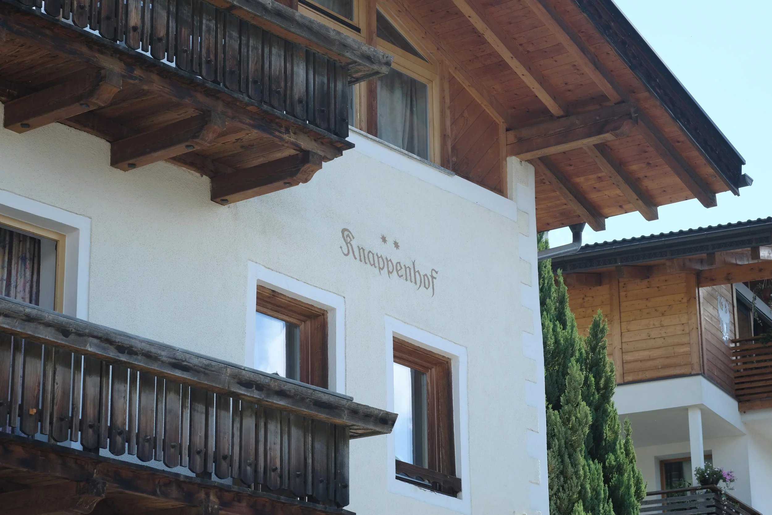 Ein mehrstöckiges Gebäude im alpinen Stil mit weißen Außenwänden, Holzdetails und Balkonen, der Name 'Sappenhof' ist an der Wand sichtbar.