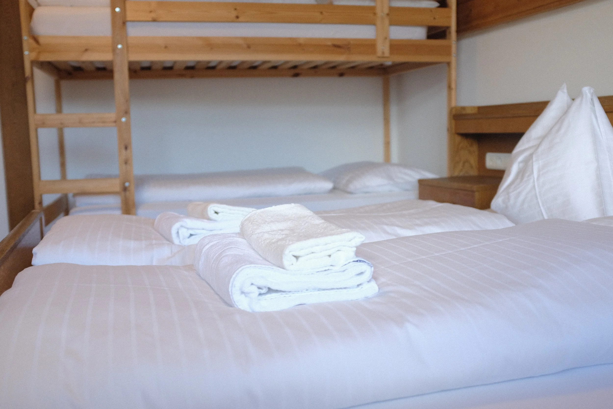Ein Bett mit weißer Bettwäsche und weißen Handtüchern, hinter einem Holzbettgestell, in einem Schlafzimmer.