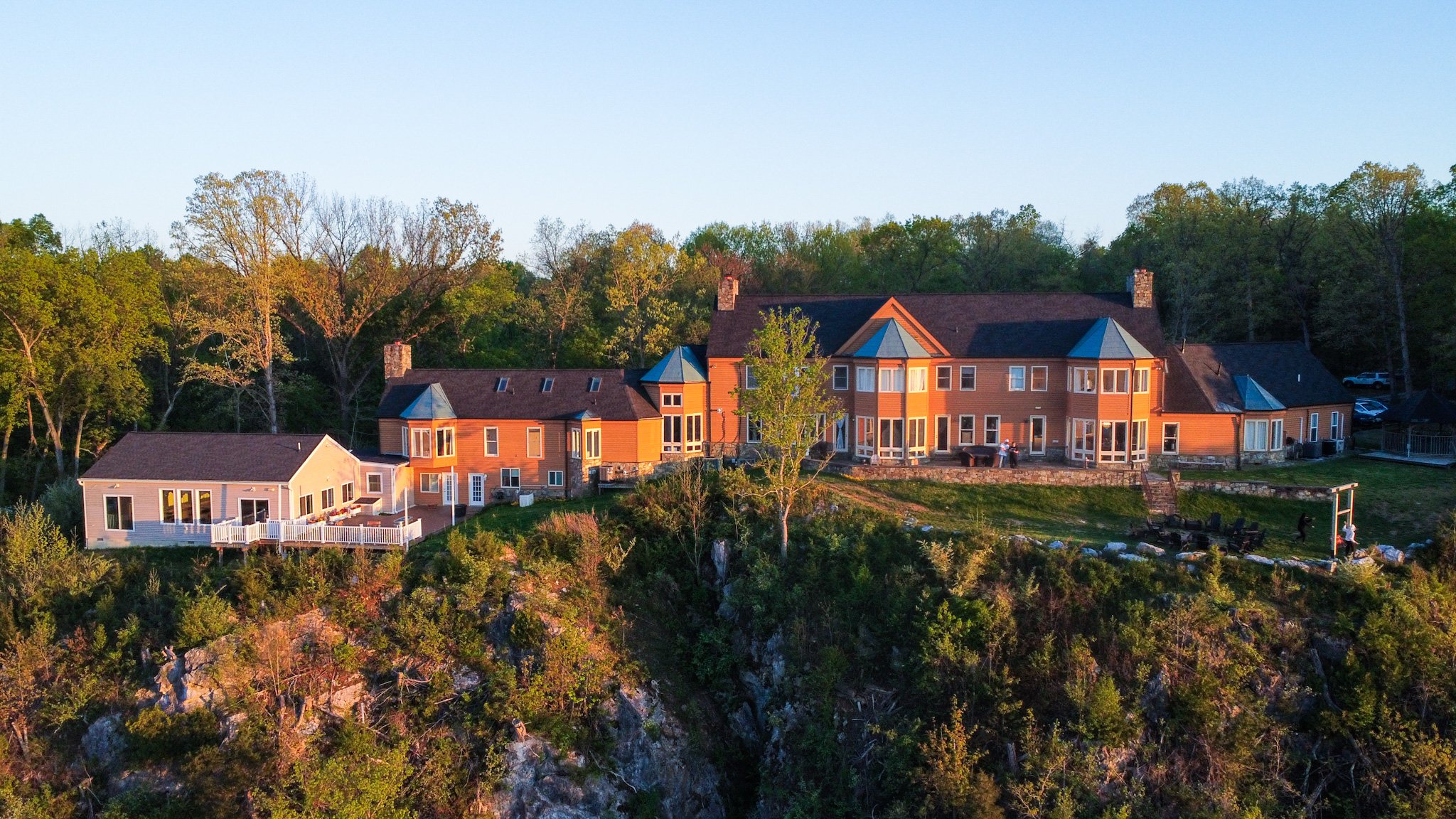 Aerial view of a large orange and brown building located on a cliff surrounded by green trees and shrubs.