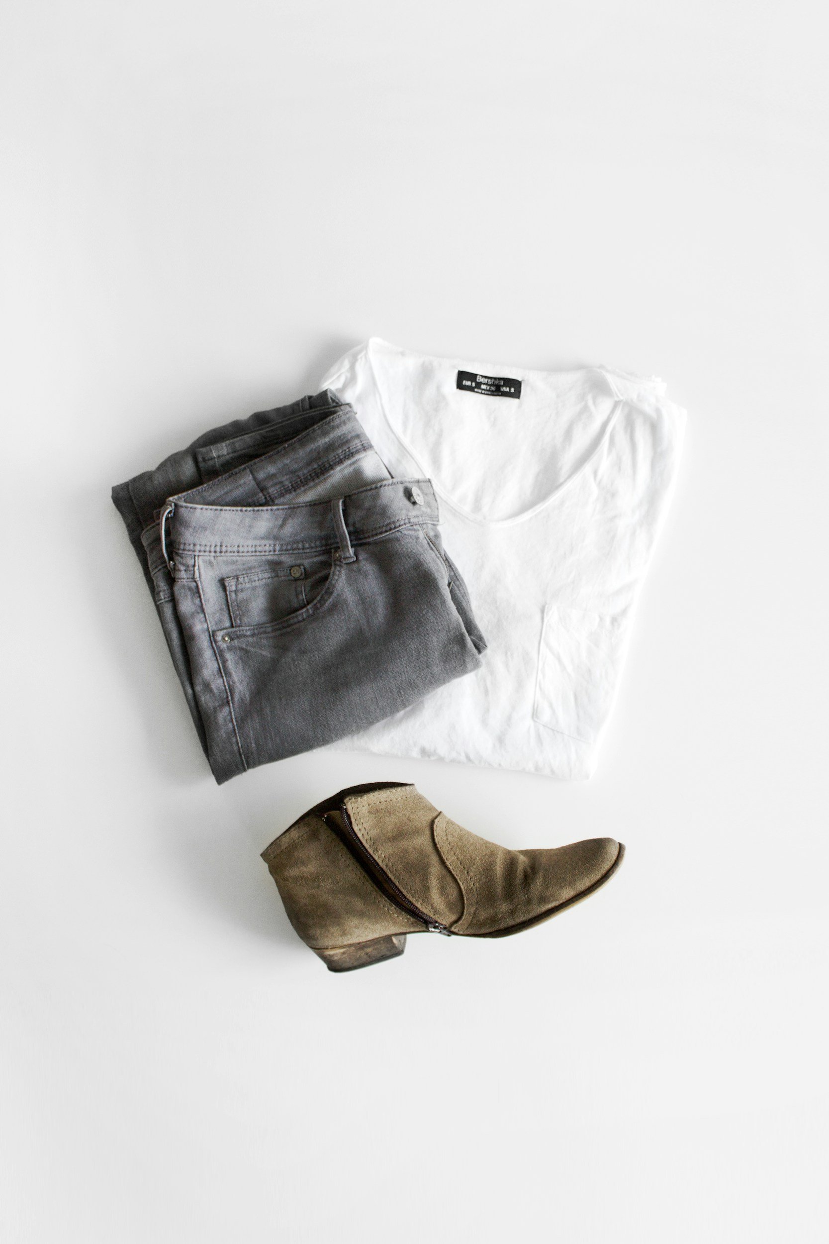 Folded white t-shirt and jeans with brown booties on a grey background.