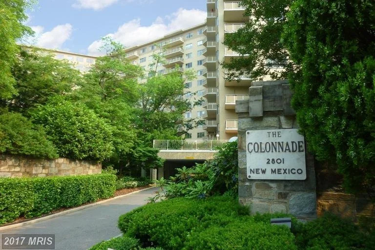 Entrance to The Colonnade apartment building with sign reading "The Colonnade 2801 New Mexico," surrounded by trees and greenery.