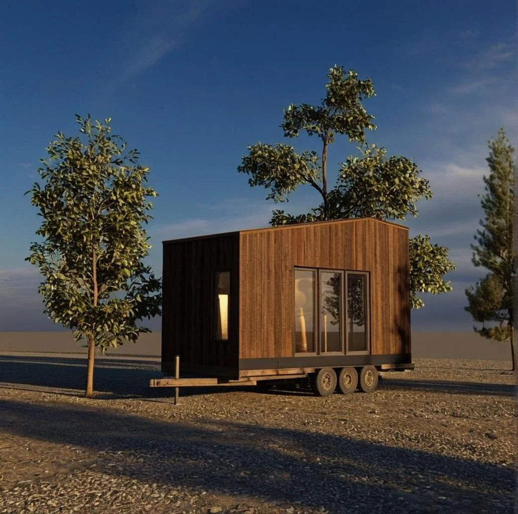 A codex tiny house on wheels with wooden siding, set on a gravel surface with trees and a blue sky in the background.