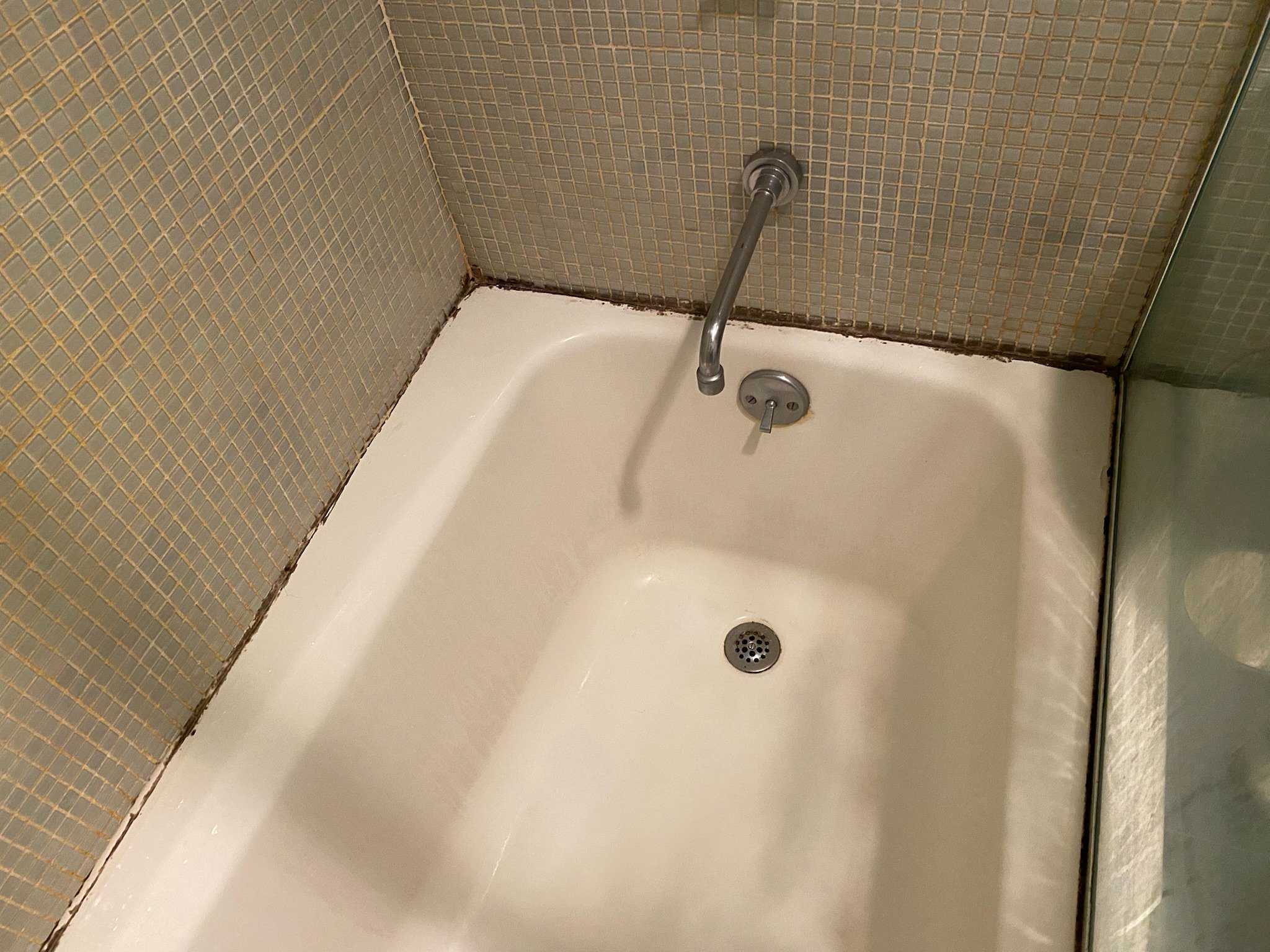 Before photo in Kips Bay showing worn bathtub with moldy grout lines: This Kips Bay tub had deep staining and deteriorated caulking around the edges. We prepped the surface for a full reseal and refinish.