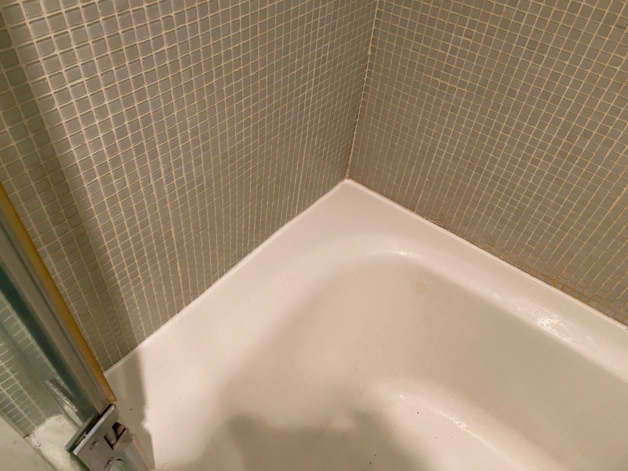 In progress photo in Kips Bay after removing old grout: Fresh caulk is applied along the tub’s perimeter, replacing cracked and moldy lines. Even halfway through, the difference is clear.