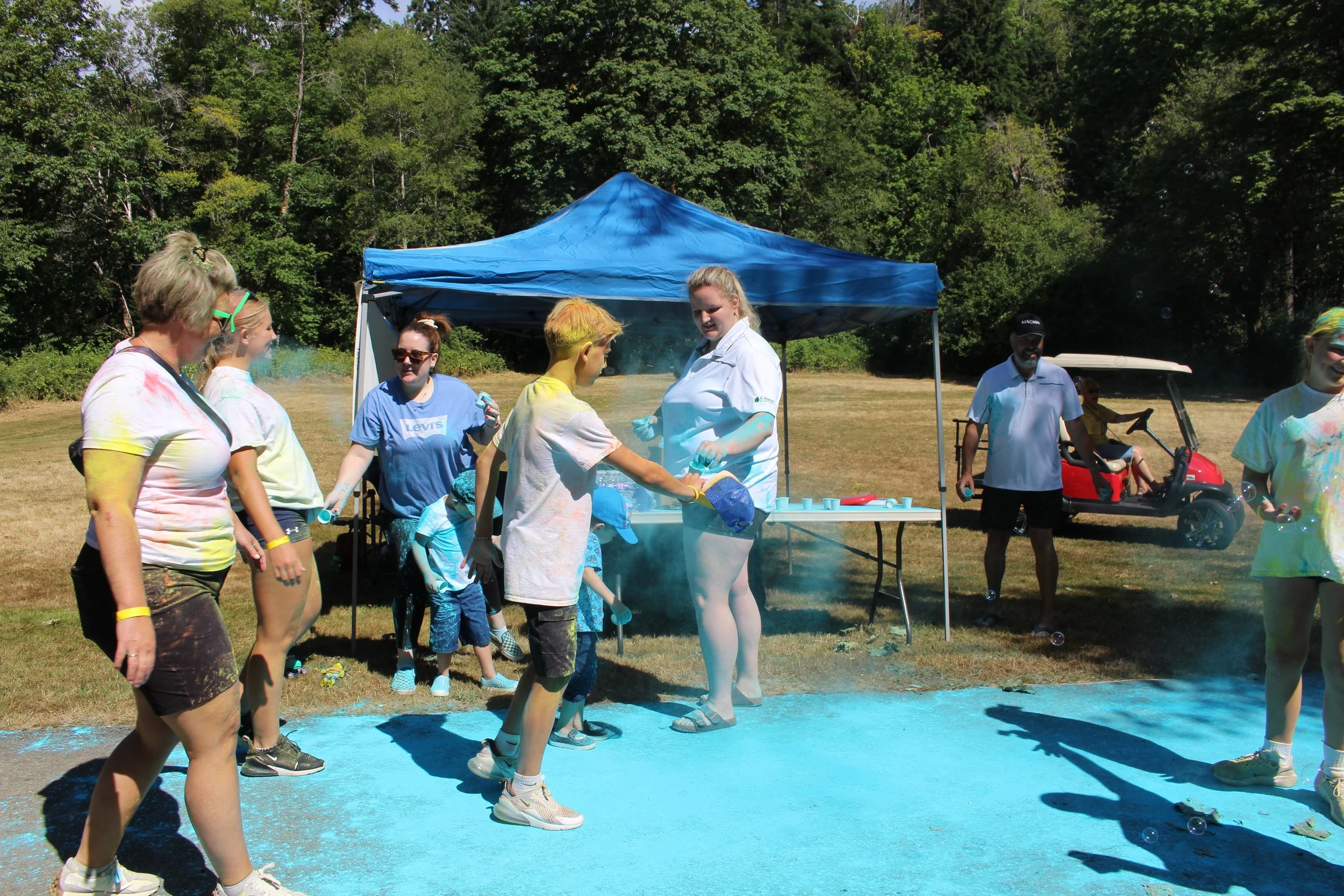 People celebrating at an outdoor color run event, with powder being thrown and colorful stains on clothing.