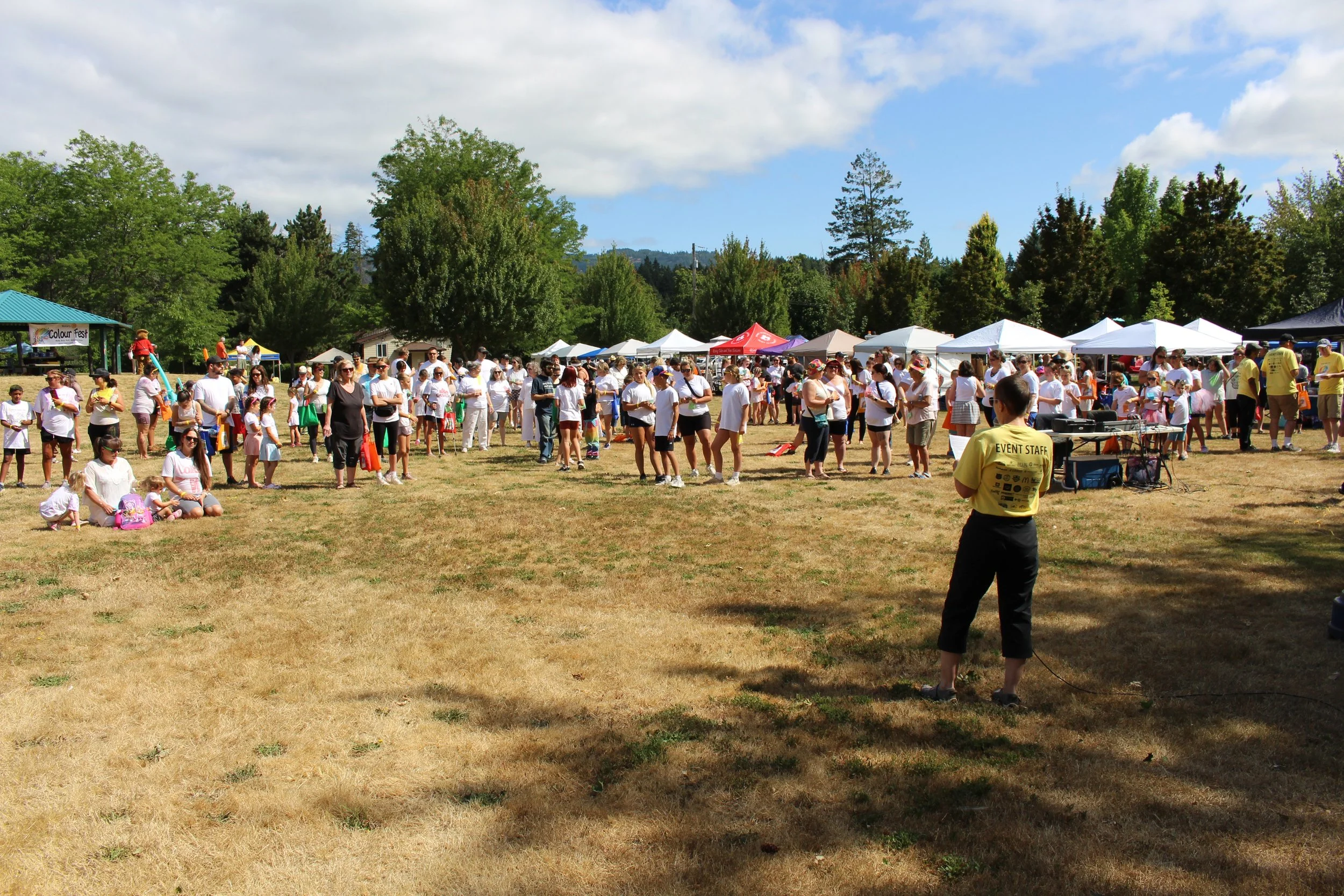 Crowd gathered with tents and trees at outdoor event on a sunny day