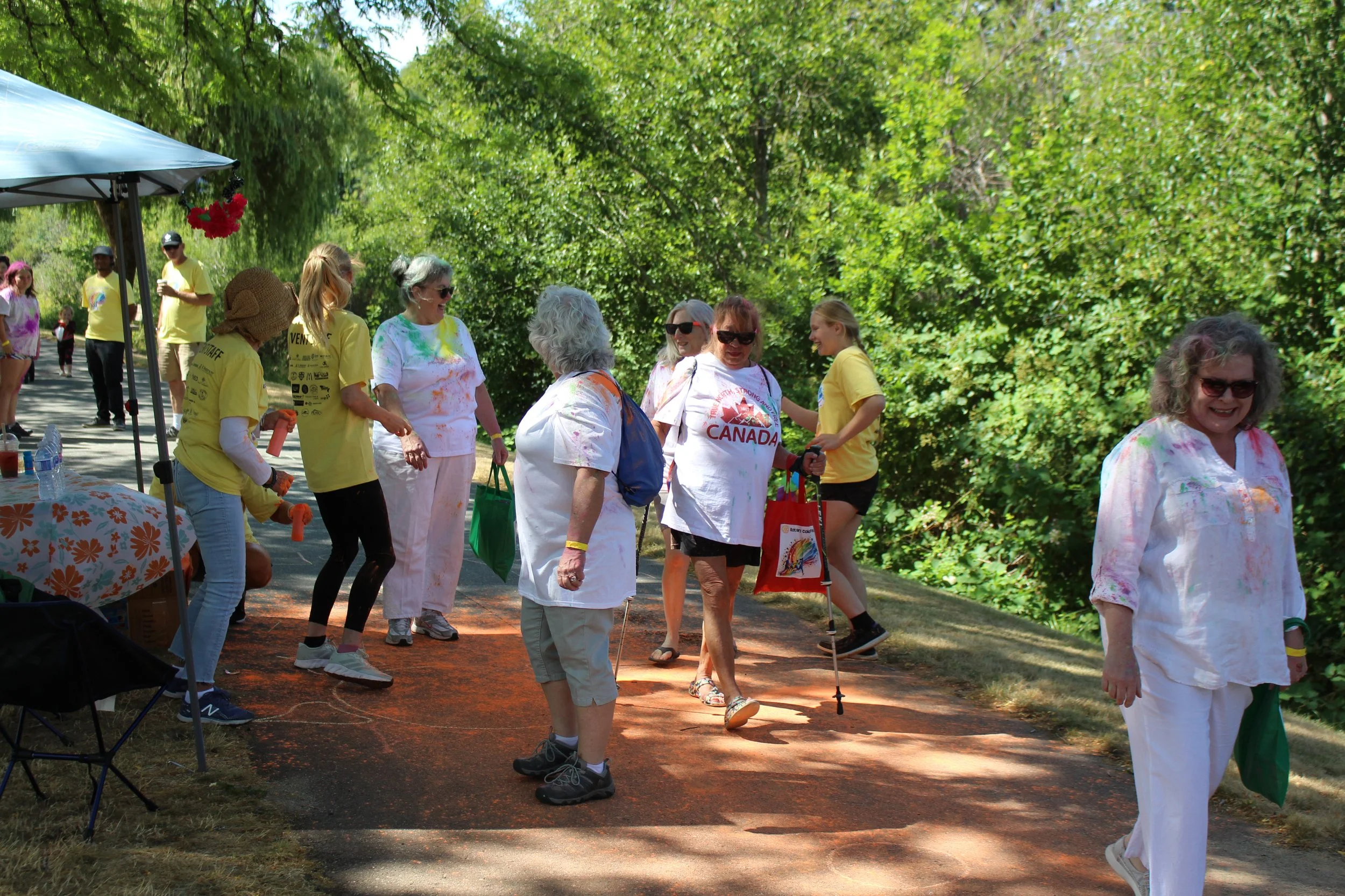 People participating in a color run, throwing colored powder on a pathway surrounded by lush green trees.