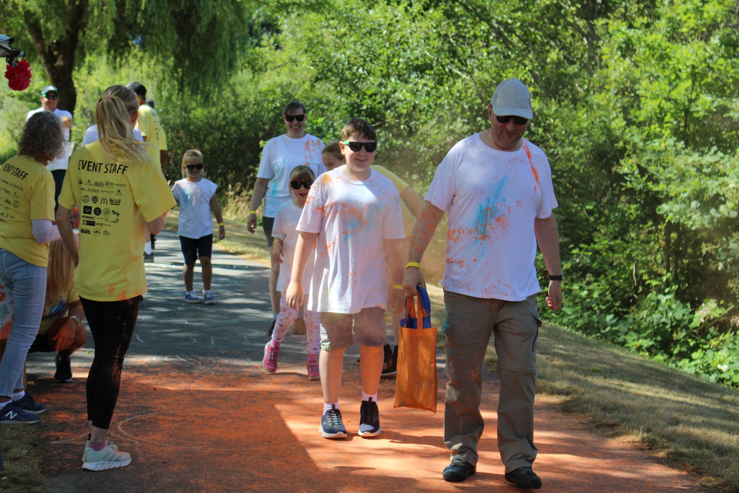 People participating in a color run event outdoors, covered in vibrant colored powders, on a sunny day with green trees in the background.