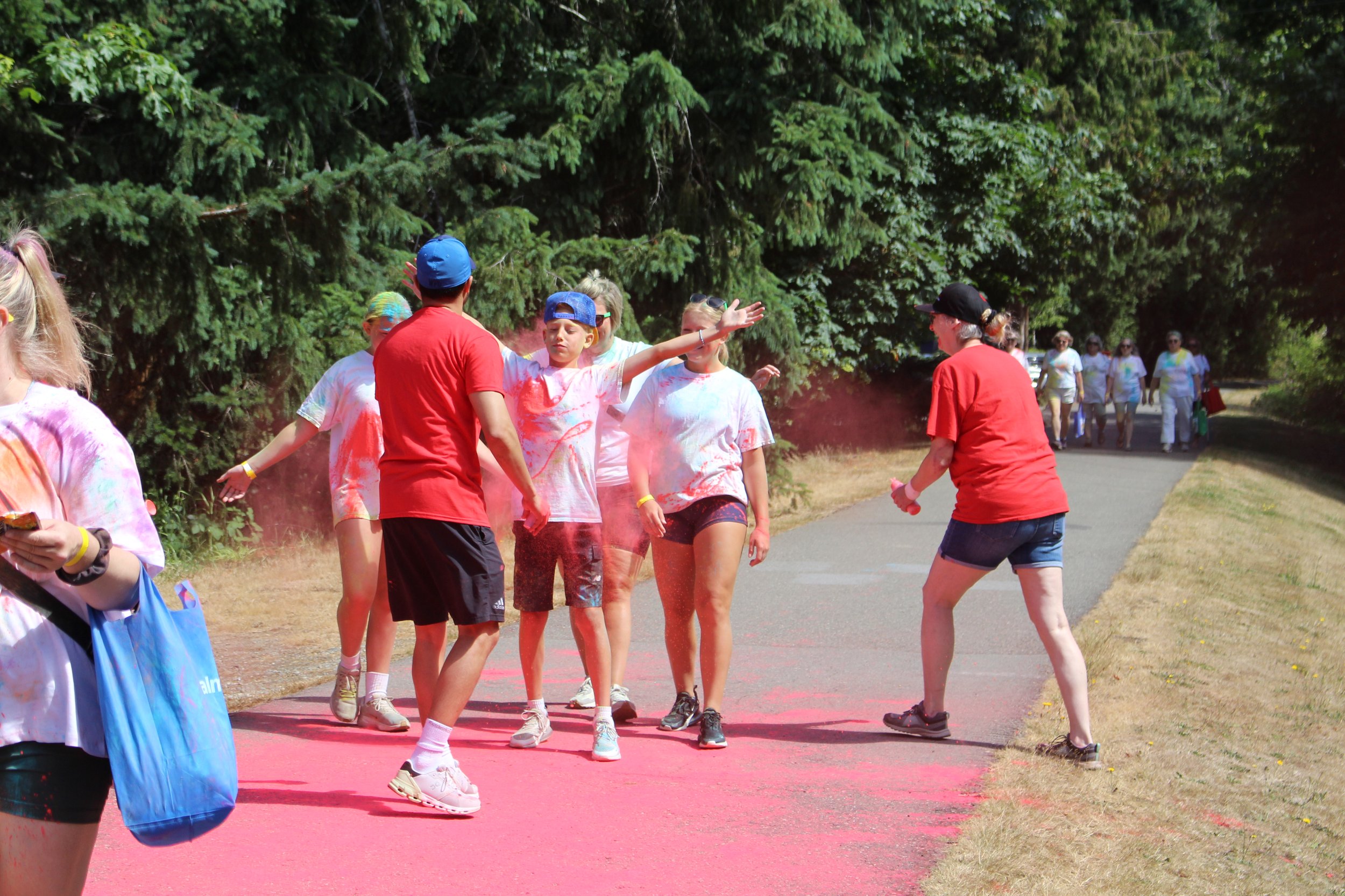 People running and playing on a pink color powder on a park path, celebrating a color run event.