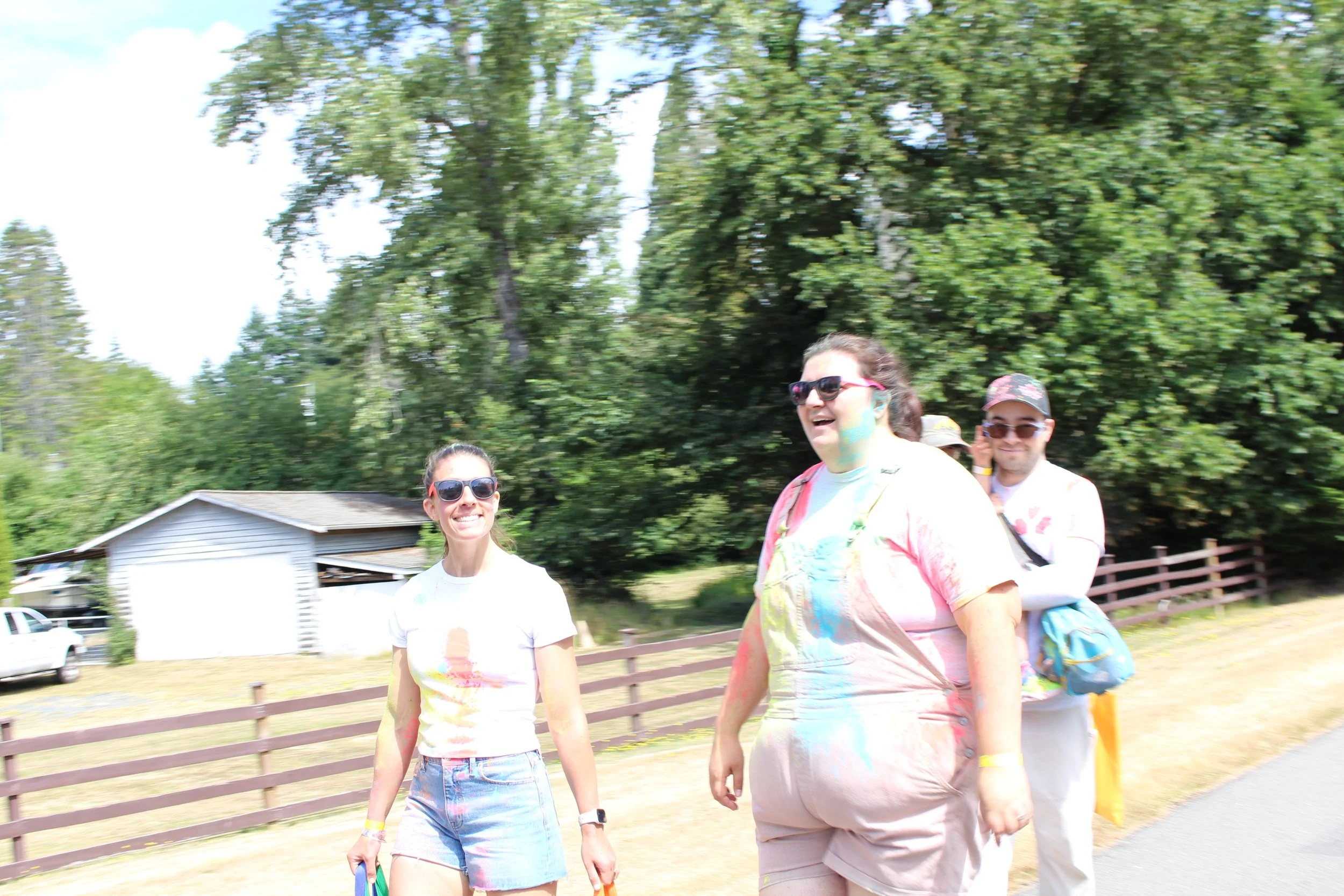 Group of friends walking outdoors in sunny weather, with trees and a wooden fence in the background.
