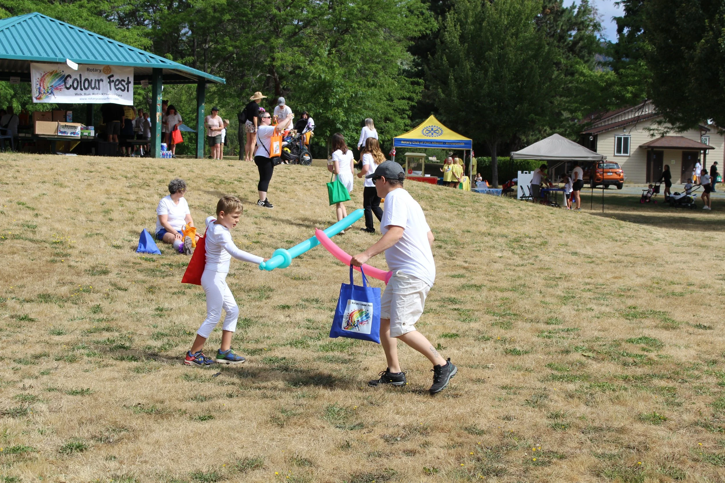 People participating in an outdoor festival on a grassy hill, with children and adults engaging in activities, tents, and booths in the background.