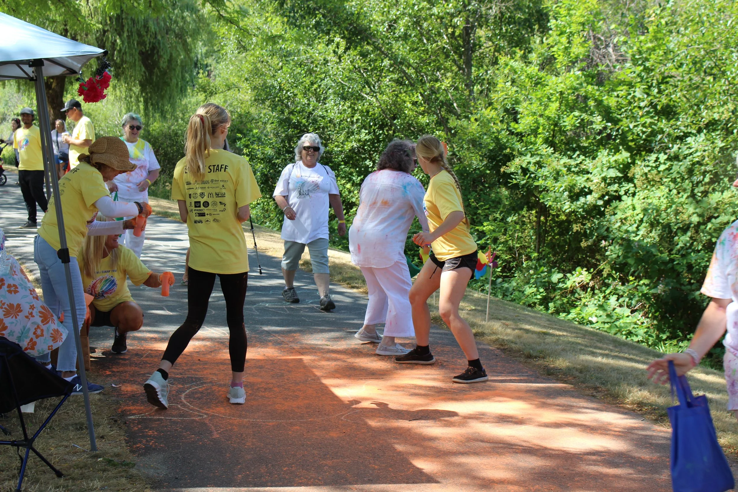 Group of people participating in a color run event outdoors, some covered in colored powder, with trees and greenery in the background.