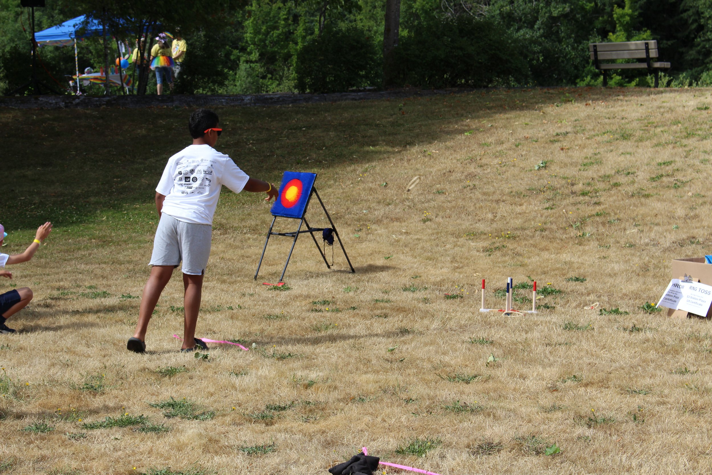 Child in a white T-shirt and shorts throwing a ring at a target during outdoor ring toss game on a grassy field