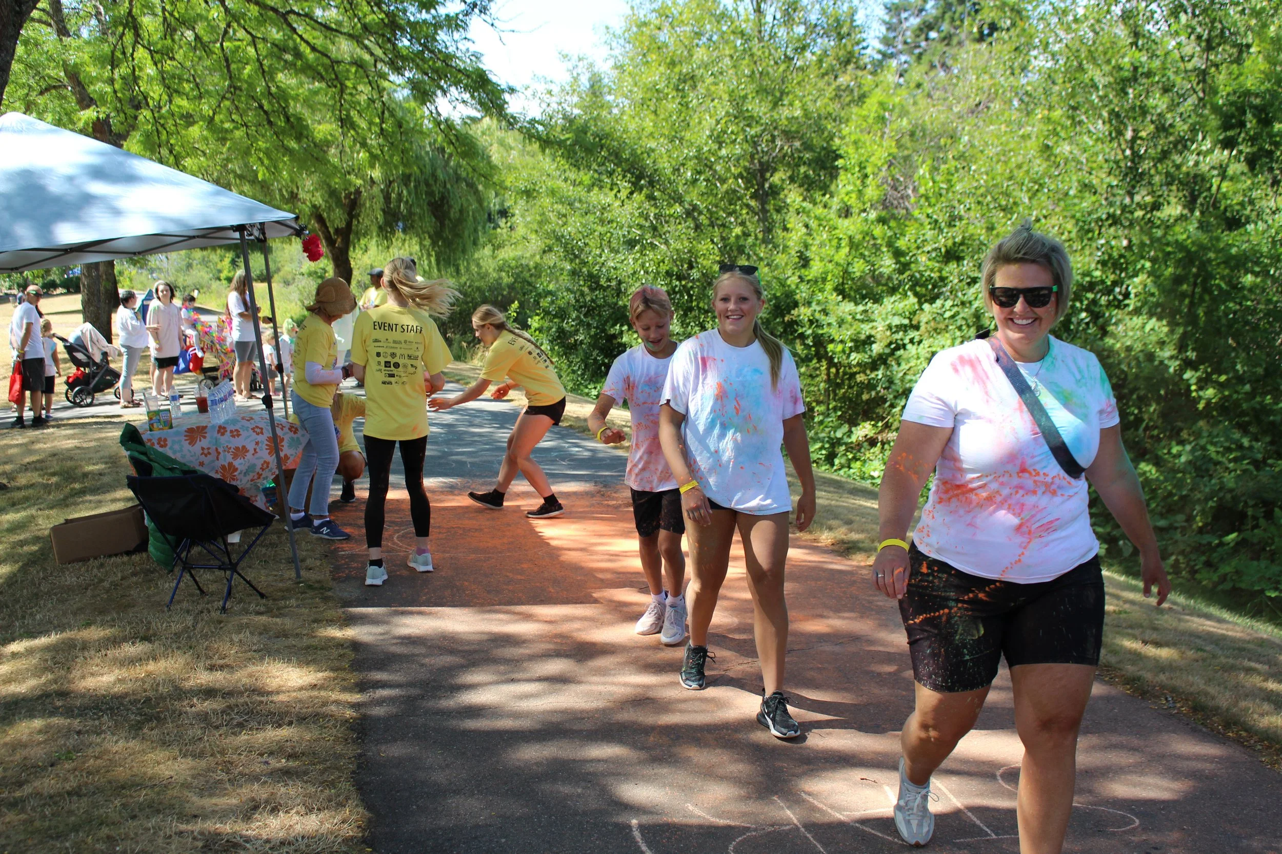 People participating in a color run event outdoors on a sunny day, covering each other with colorful powder.
