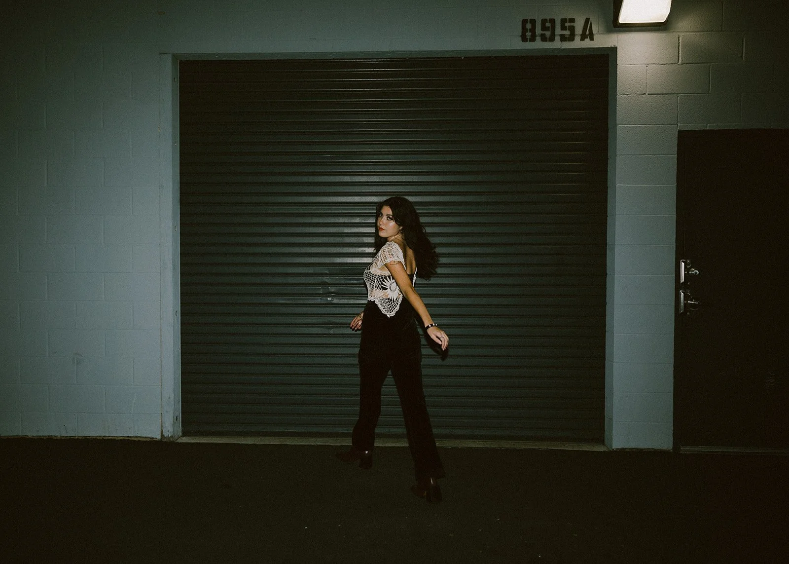 Woman with long dark hair walking in a crochet top against garage at night — Edgy fashion portrait session in Orange County — Captured by Tesla Rae Photo