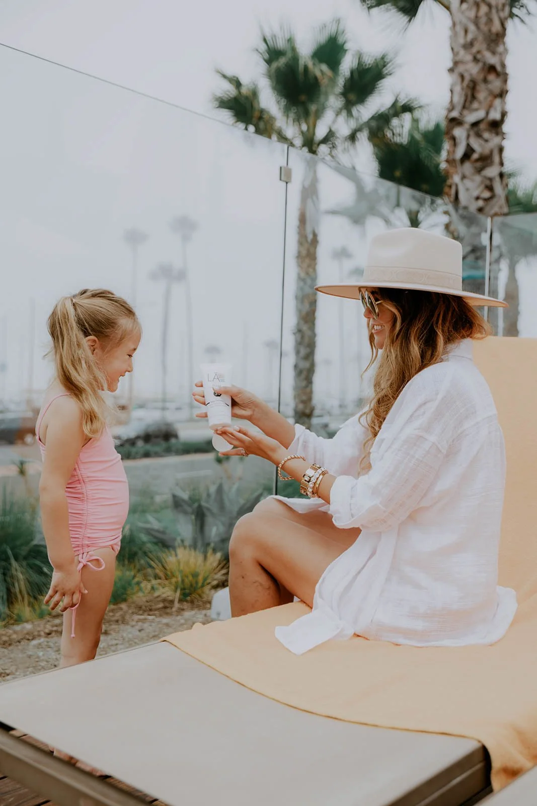 Lifestyle branding photo of a mother and daughter by the pool in Newport Beach, California featuring natural skincare product content creation with a relaxed coastal luxury aesthetic.