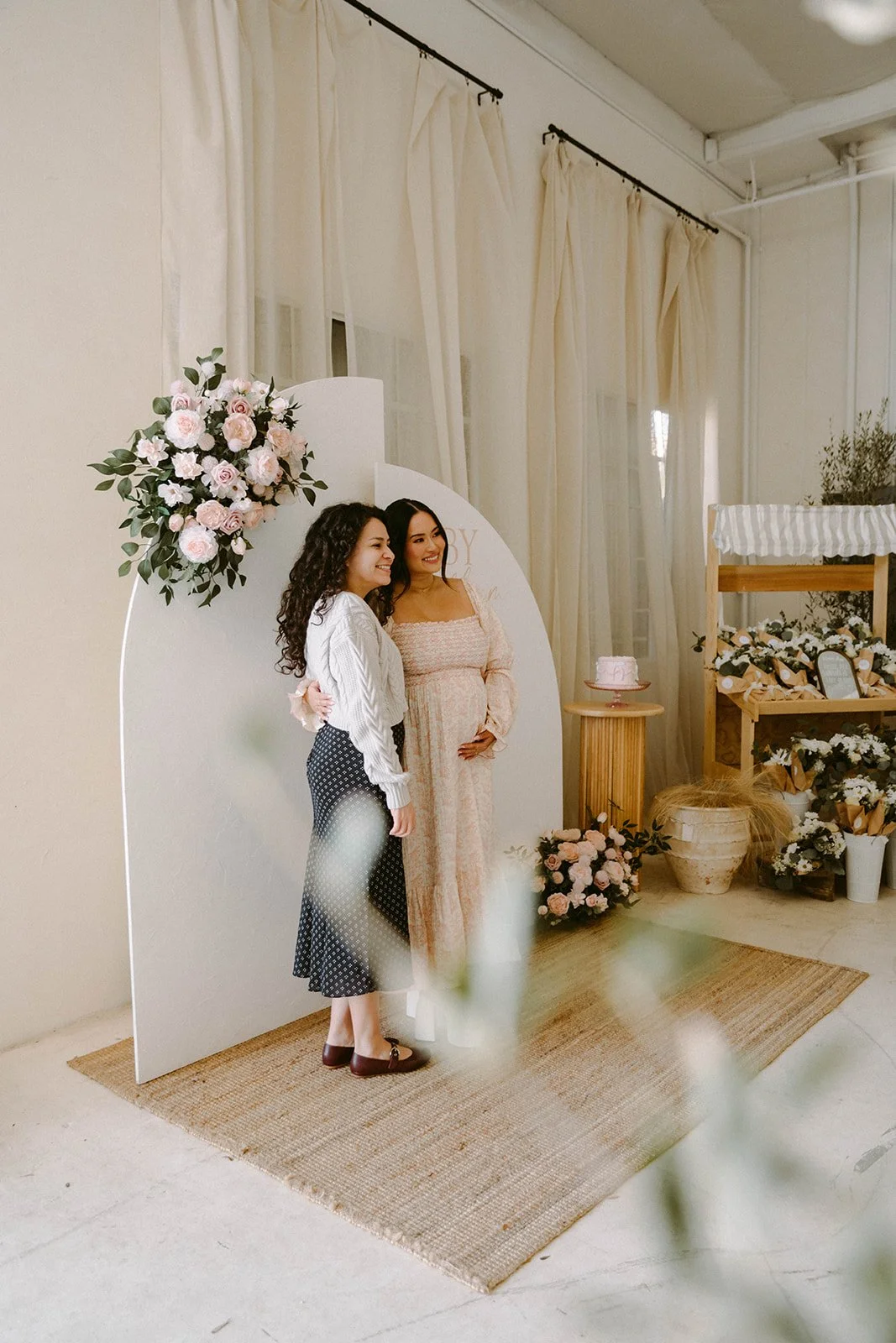 Candid shot of pregnant women with her party guest posing in front of a photo backdrop at baby shower at Still Interior event space in Costa Mesa — Orange County event photographer Tesla Rae Photo