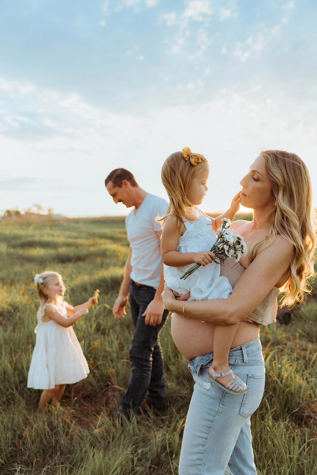 Pregnant mother holding her daughter at sunset in green, golden field in Costa Mesa — Best maternity photographers in Orange County — Tesla Rae Photo