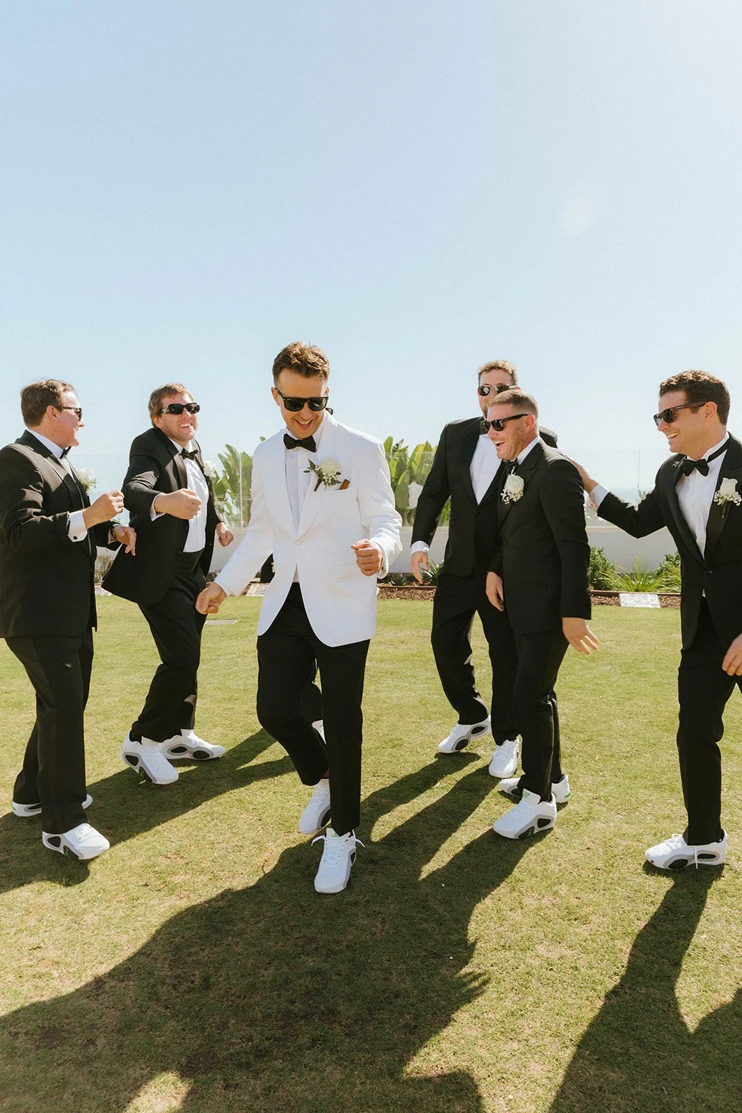 Groomsmen in black tuxedos and sunglasses celebrating together at Halo Rooftop Bar at Fairmont Breakers Long Beach overlooking the Queen Mary in Long Beach, California. Editorial-style wedding photography with modern coastal luxury vibes.