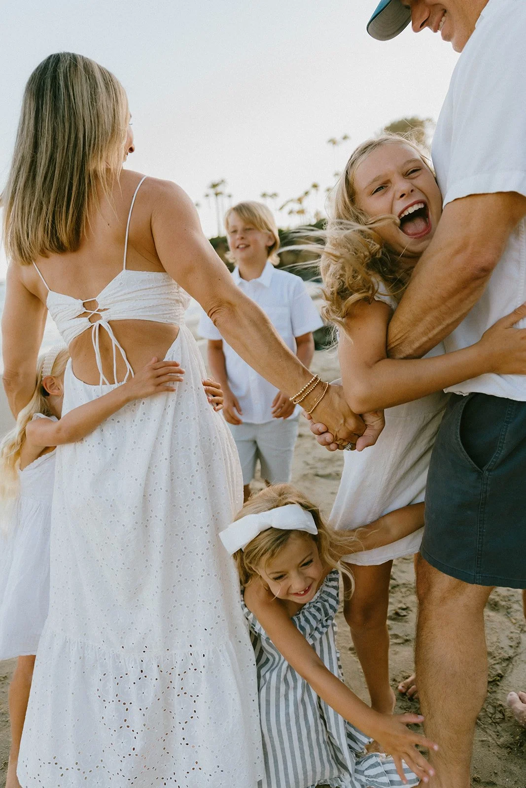 A father tossing his young daughter into the air while the family enjoys a golden hour beach session in Huntington Beach, California. Candid coastal family photography with warm sunset light and playful natural moments.