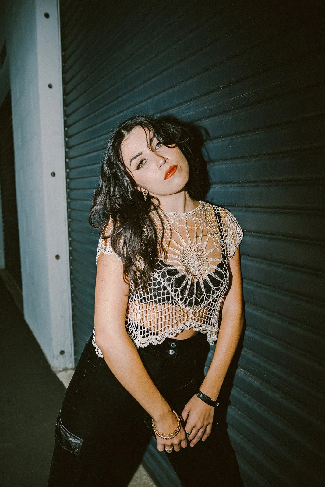 Woman with long dark hair posing in a crochet top against garage at night — Edgy fashion portrait session in Orange County — Captured by Tesla Rae Photo