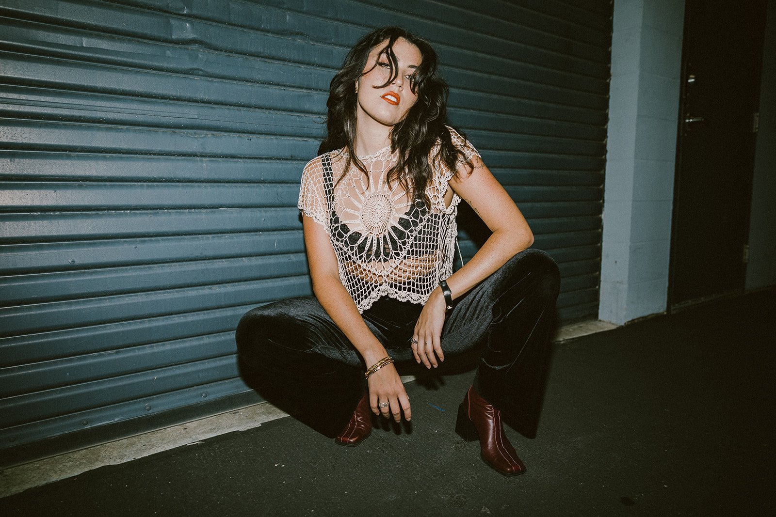 Woman with long dark hair posing in a crochet top against garage at night — Edgy fashion portrait session in Orange County — Captured by Tesla Rae Photo
