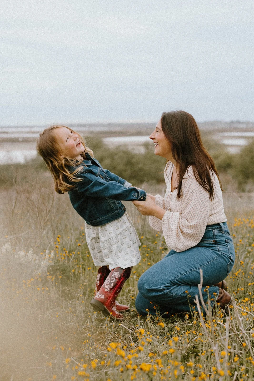 Little girl wearing red, cowboy boots laughing and playing at golden field in Huntington Beach — Best candid family photographers in Huntington Beach — Captured by Tesla Rae Photo