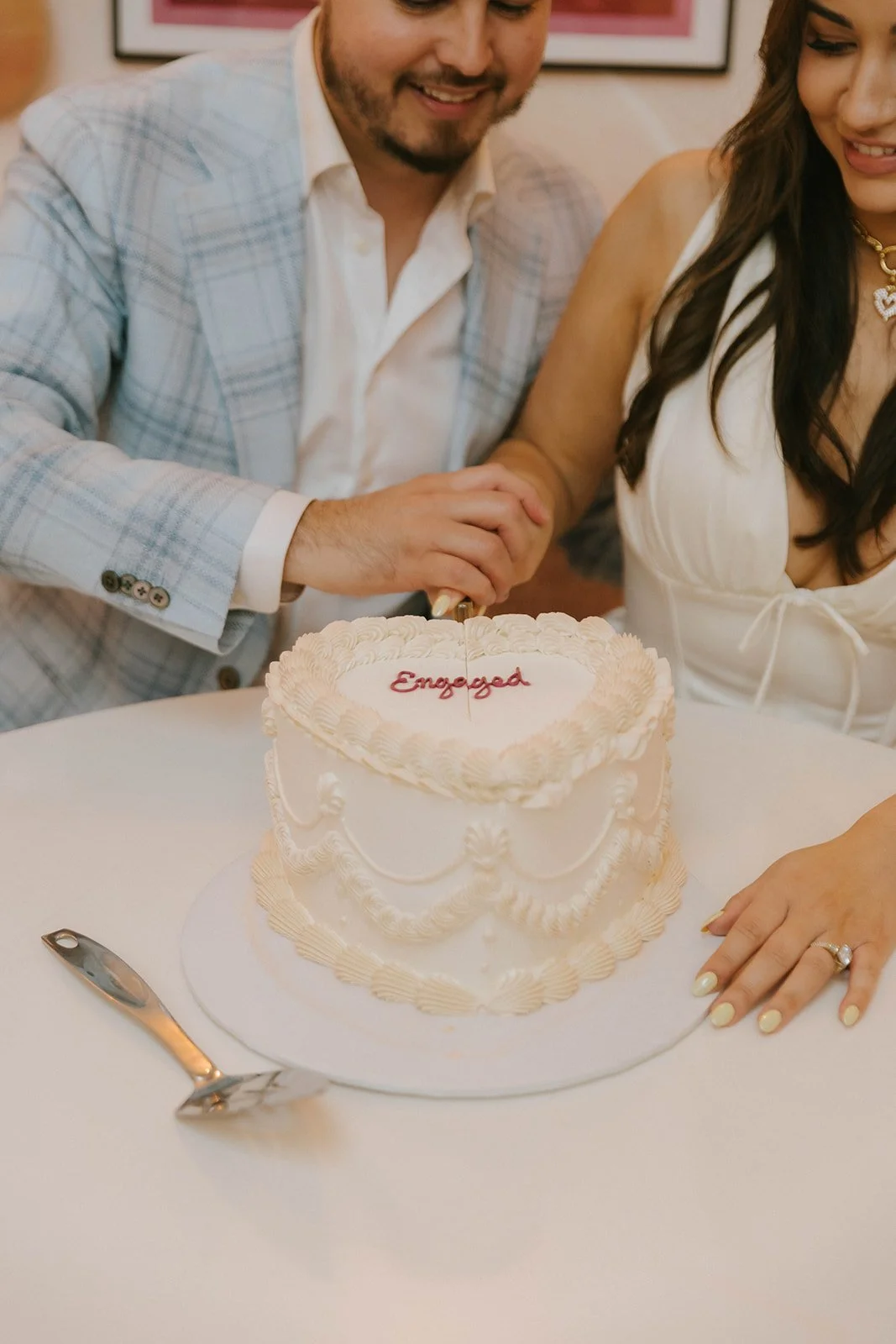 A newly engaged couple cutting a wedding cake with the word "Engaged" written on it.