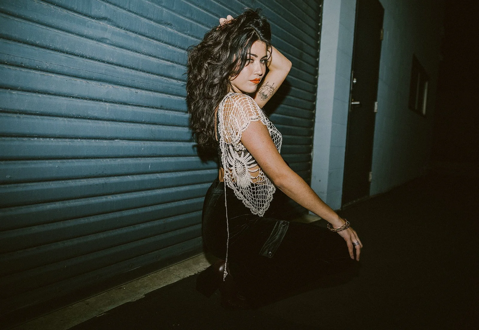 Woman with long dark hair posing in a crochet top against garage at night — Edgy fashion portrait session in Orange County — Captured by Tesla Rae Photo