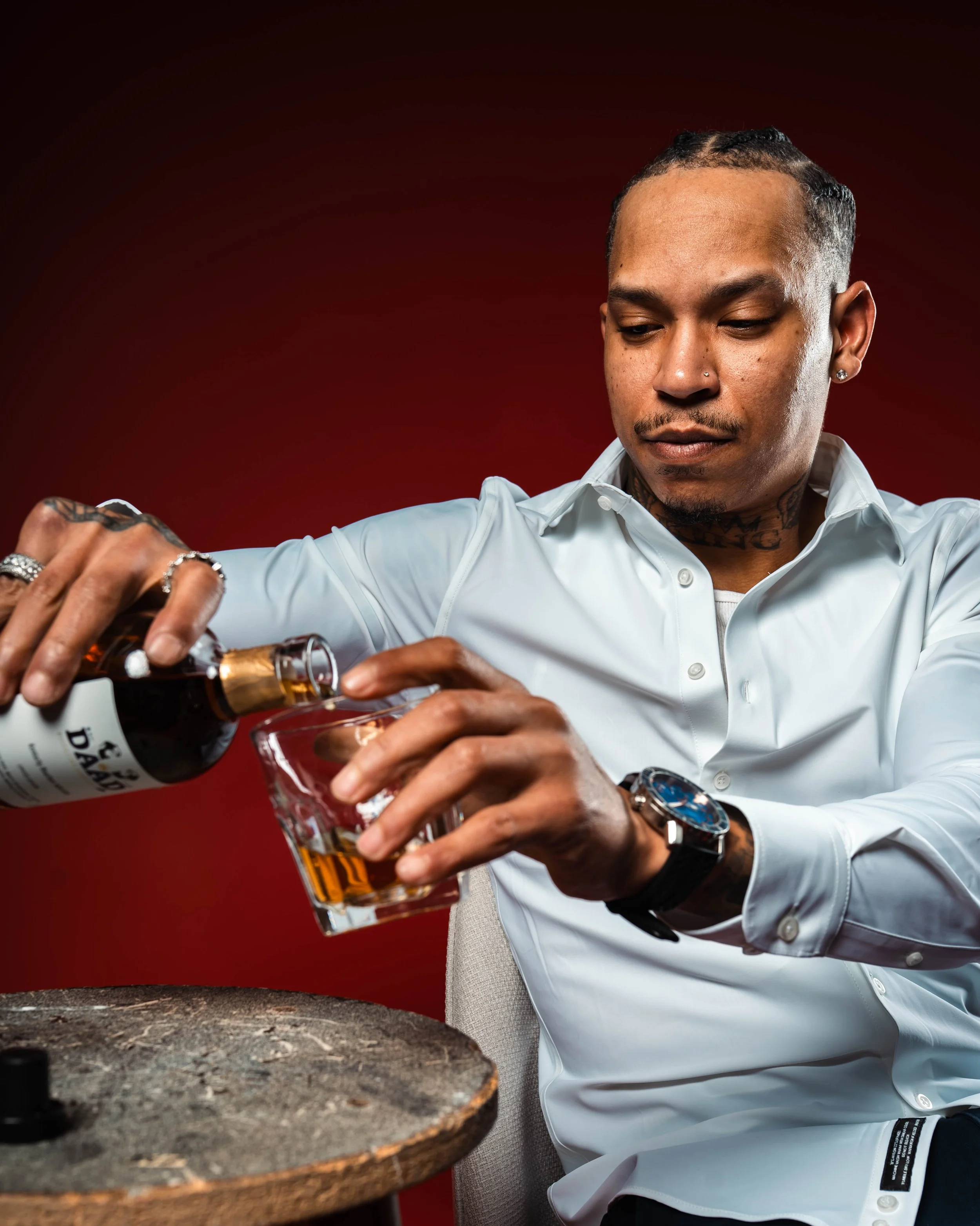 Man in a white shirt pouring whiskey into a glass on a dark red background.