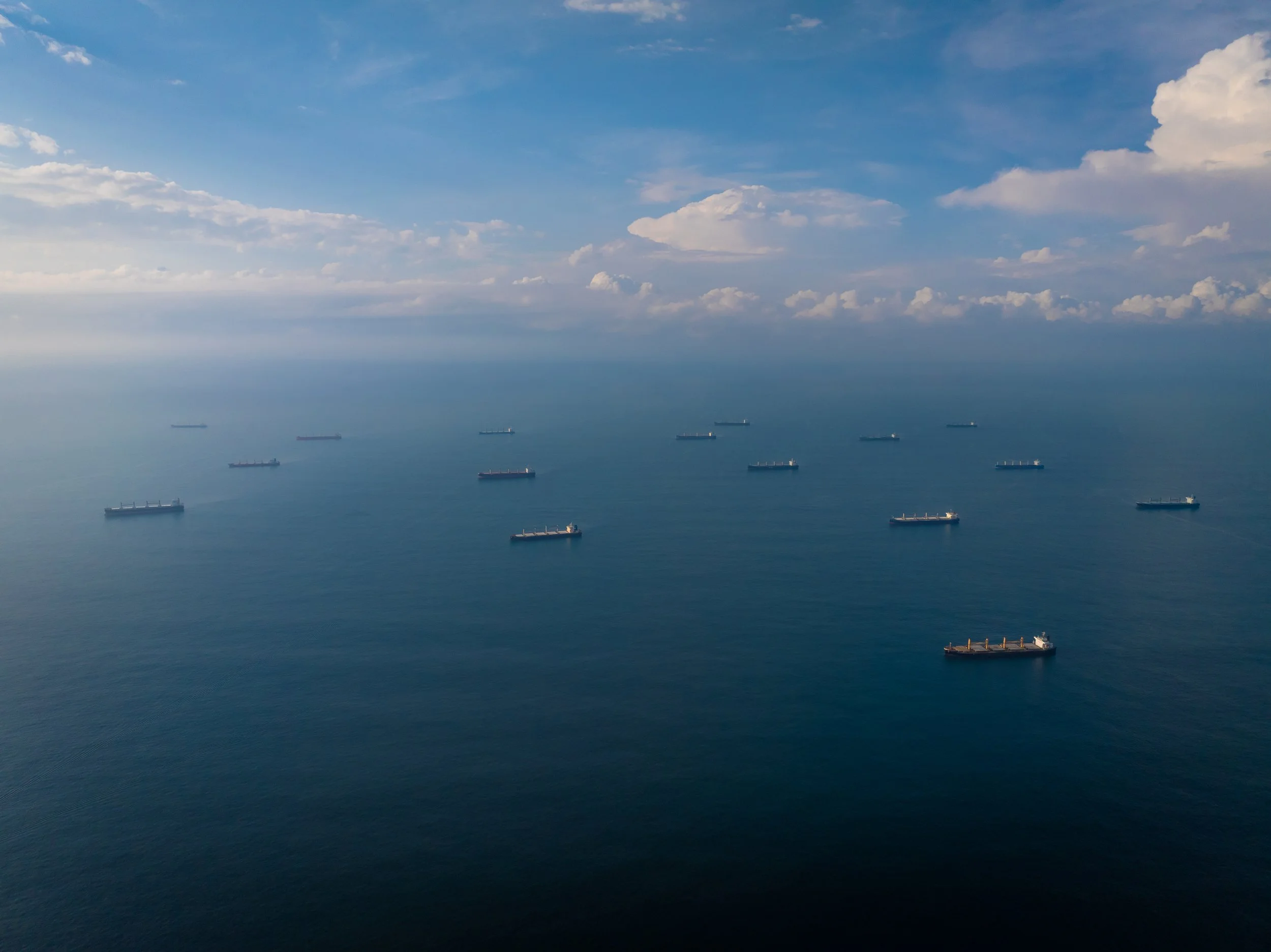 Vista aérea del océano con varios barcos de carga distribuidos en el mar, cielo con nubes dispersas.