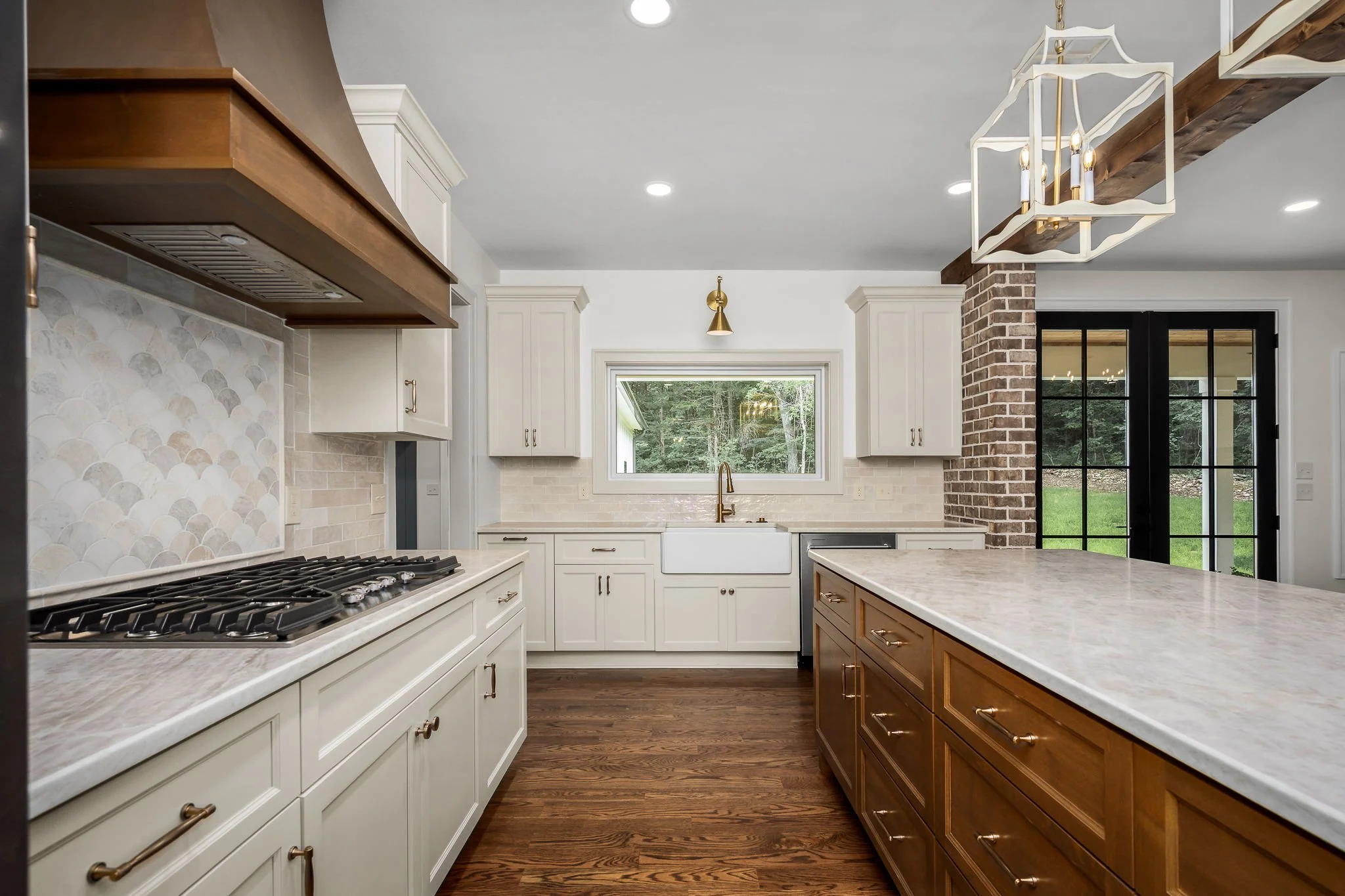 Modern kitchen with white cabinets, a large island with a light-colored countertop, a brick accent wall, a window above the sink, and a view of greenery outside.