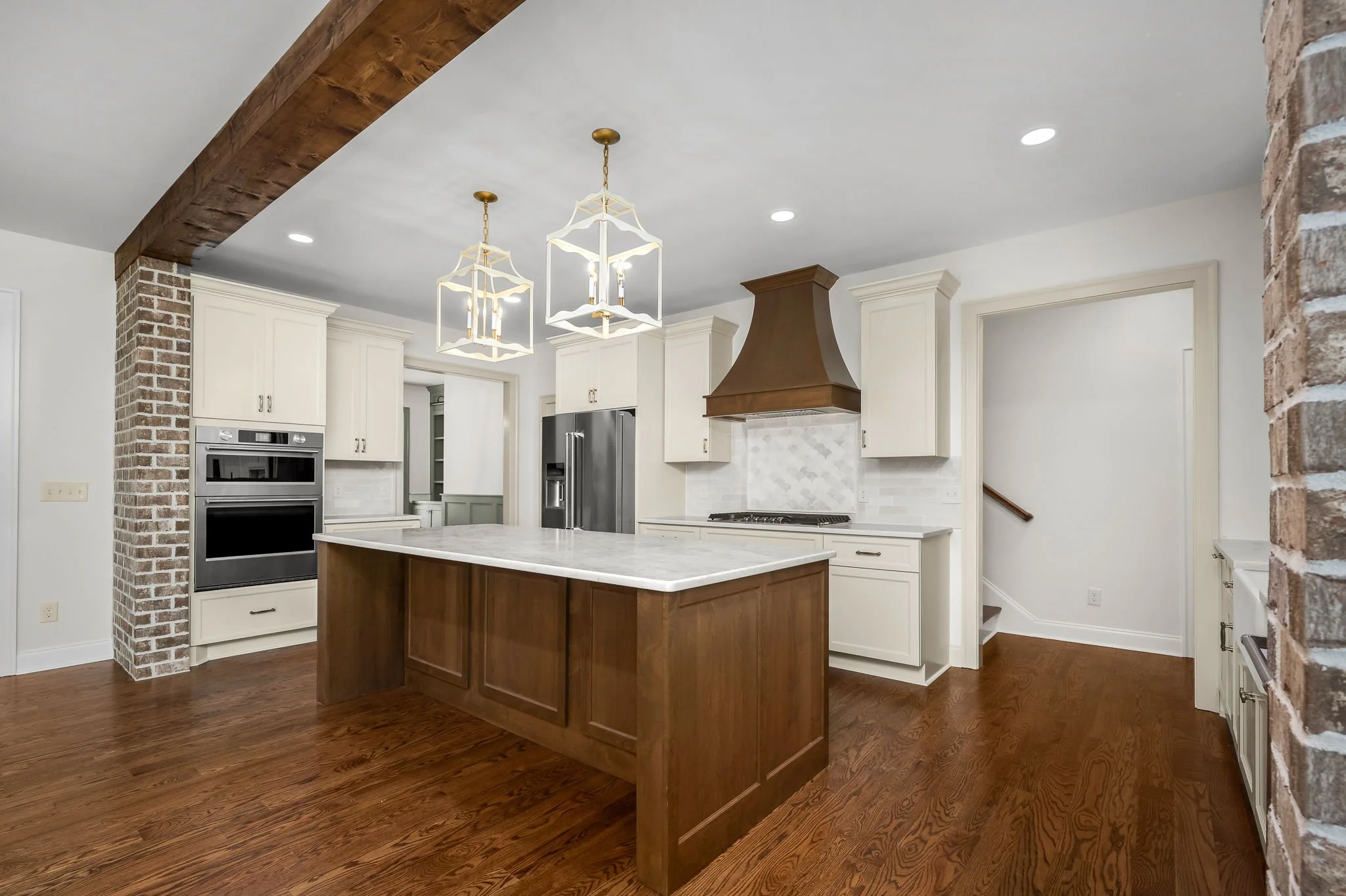 Modern kitchen with white cabinets, a large wooden island with a white marble countertop, brick accents, and two pendant lights hanging from the ceiling.