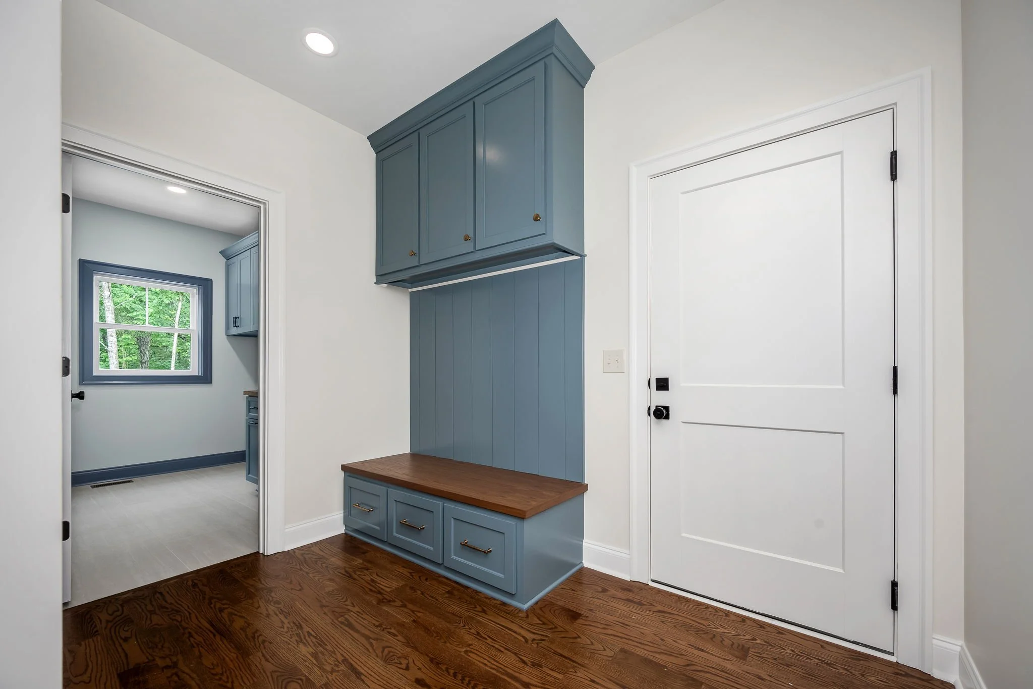 Entryway with white door, blue coat hooks and storage cabinet, hardwood floors, and a window showing greenery outside.