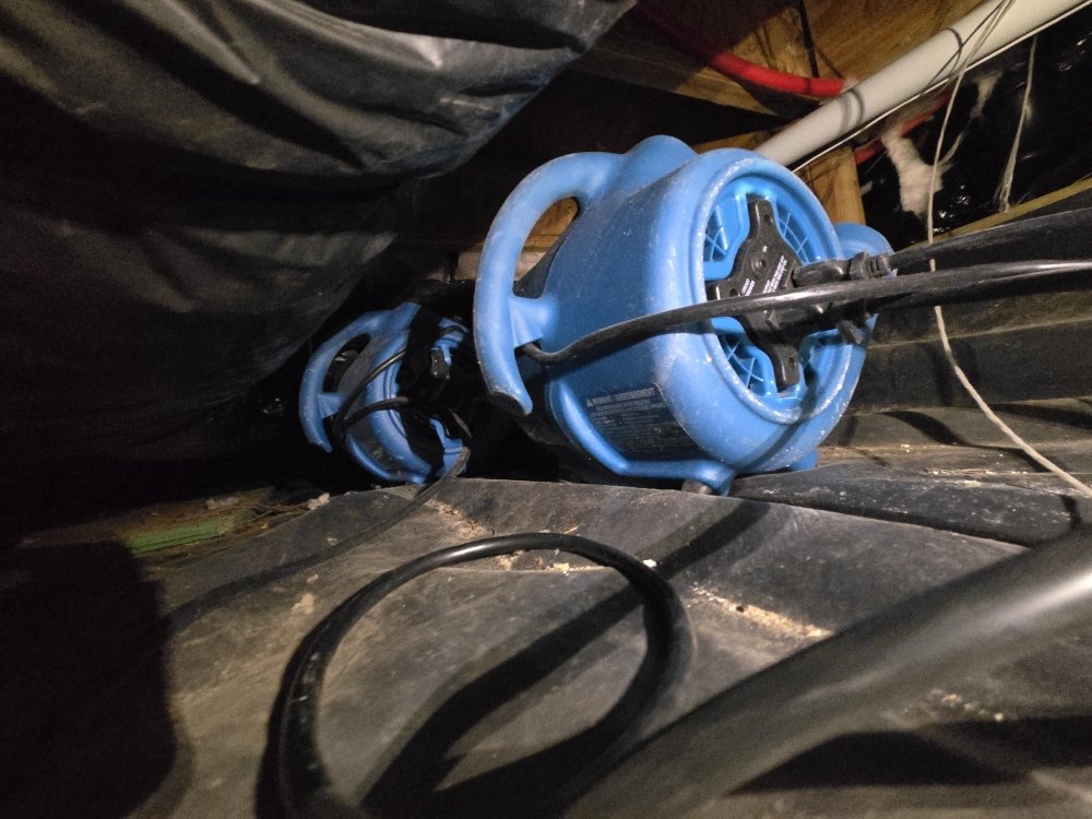 Two blue industrial air movers run on a black plastic-covered floor, part of our crawlspace drying service in Portland OR.