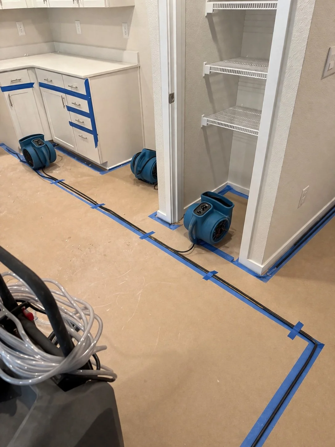Three blue air movers—drying equipment used on water damage to flooring—dry a taped-off kitchen and pantry under renovation.