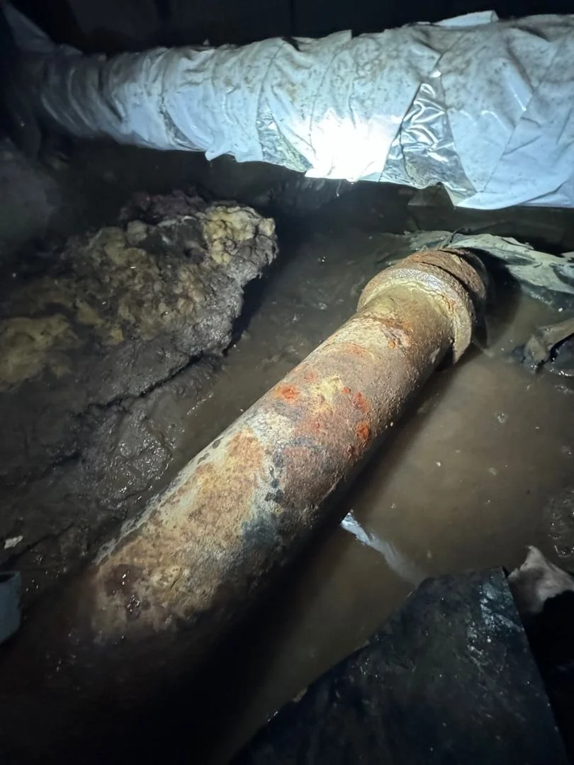 A rusty pipe in muddy water, debris scattered, and old insulation above—possible spot for sewage cleanup in Portland Oregon.