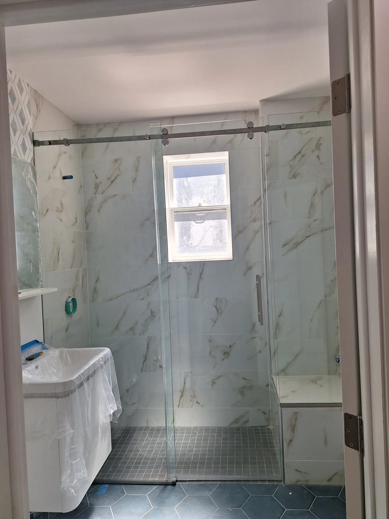 Modern bathroom with a glass shower enclosure, a window, and a small sink.
