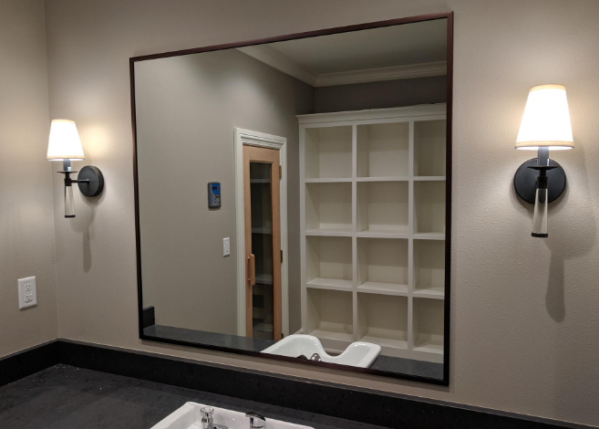 Two workers in face masks installing or repairing a wall or ceiling in a room with hardwood floors and large windows.
