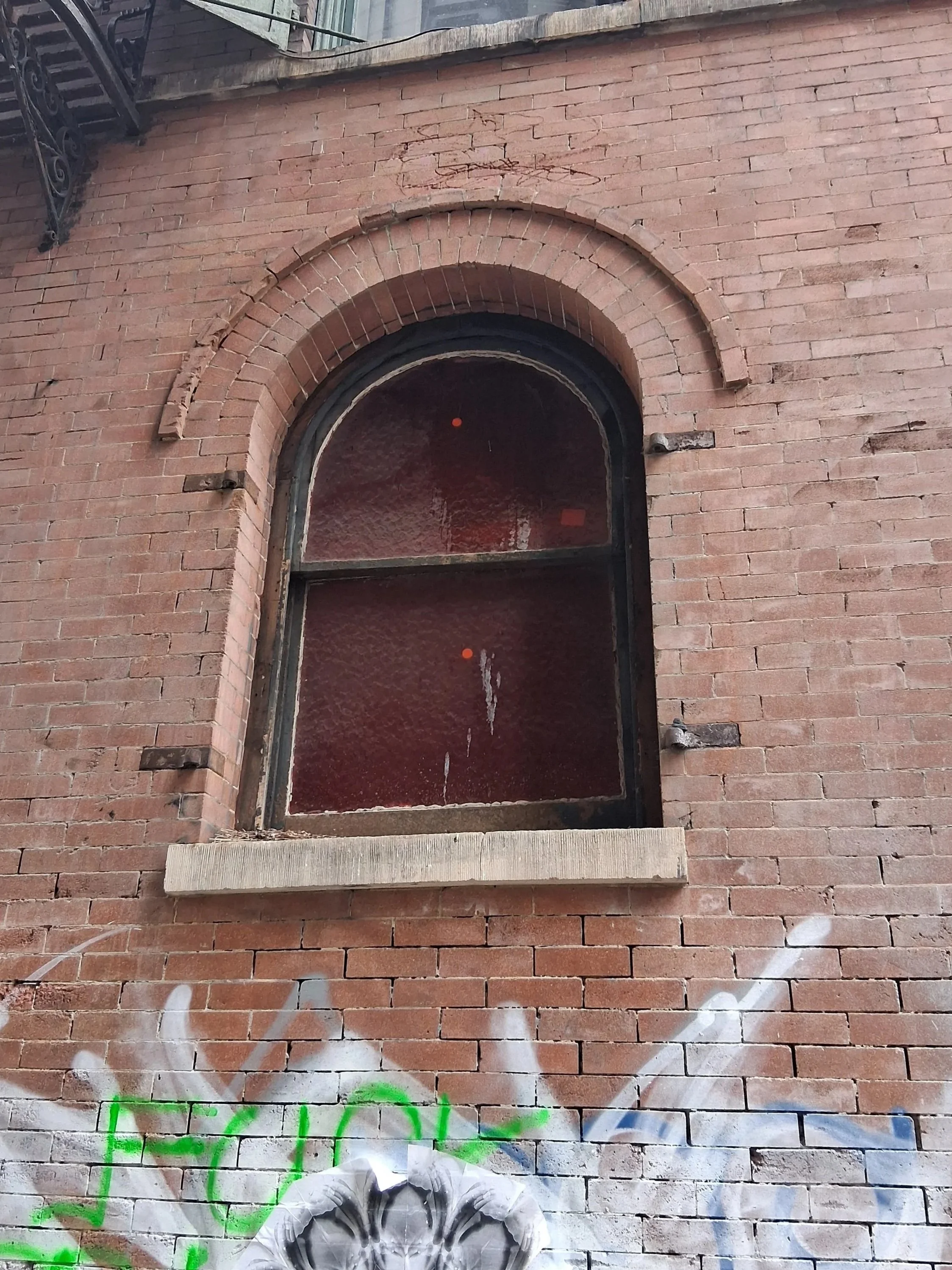 A building with a decorative arched window framed with white molding and a window sill, set against a beige textured wall.