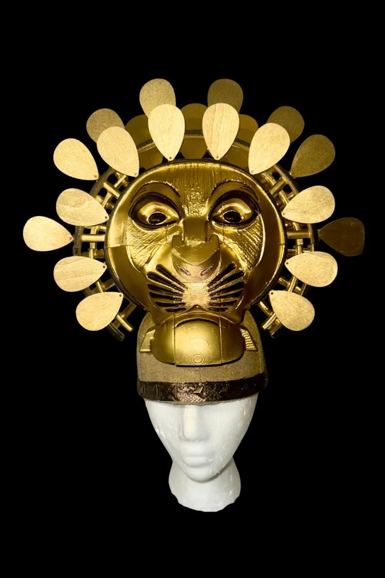 Handmade gold lion headdress featuring a stylized lion face surrounded by radiating gold mane pieces, displayed on a mannequin head for The Lion King JR. musical.