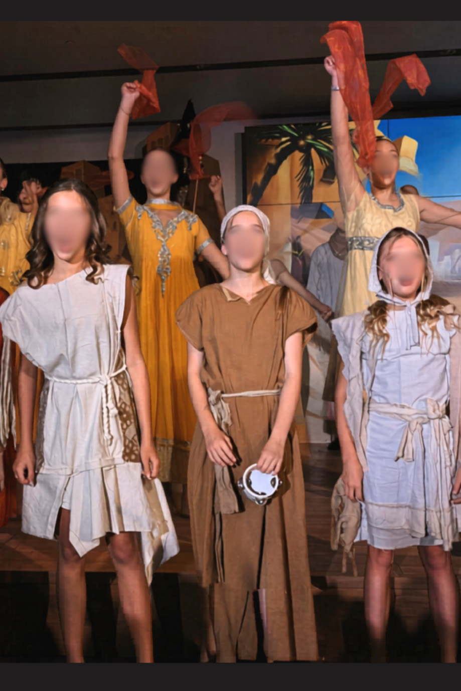 Agrabah beggar ensemble in Aladdin Jr wearing neutral-toned costumes, standing on stage during a school musical performance scene.