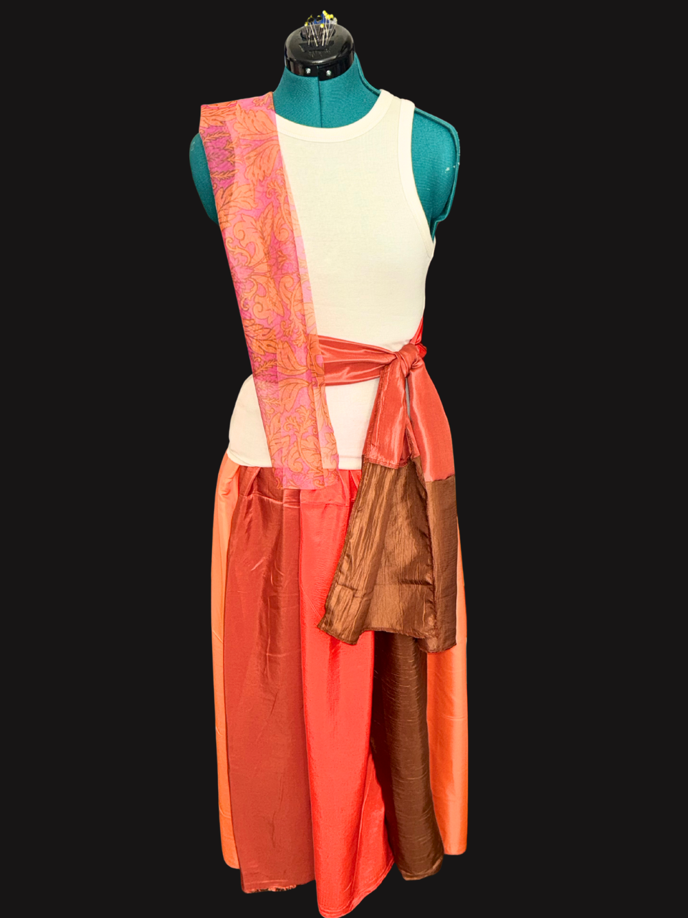 Arabian dancer costume detail for Aladdin Jr showing cream tank top, coral sash, patterned scarf, and multi-colored satin skirt of rust, light orange, dark orange, brown, panels for school musical production.