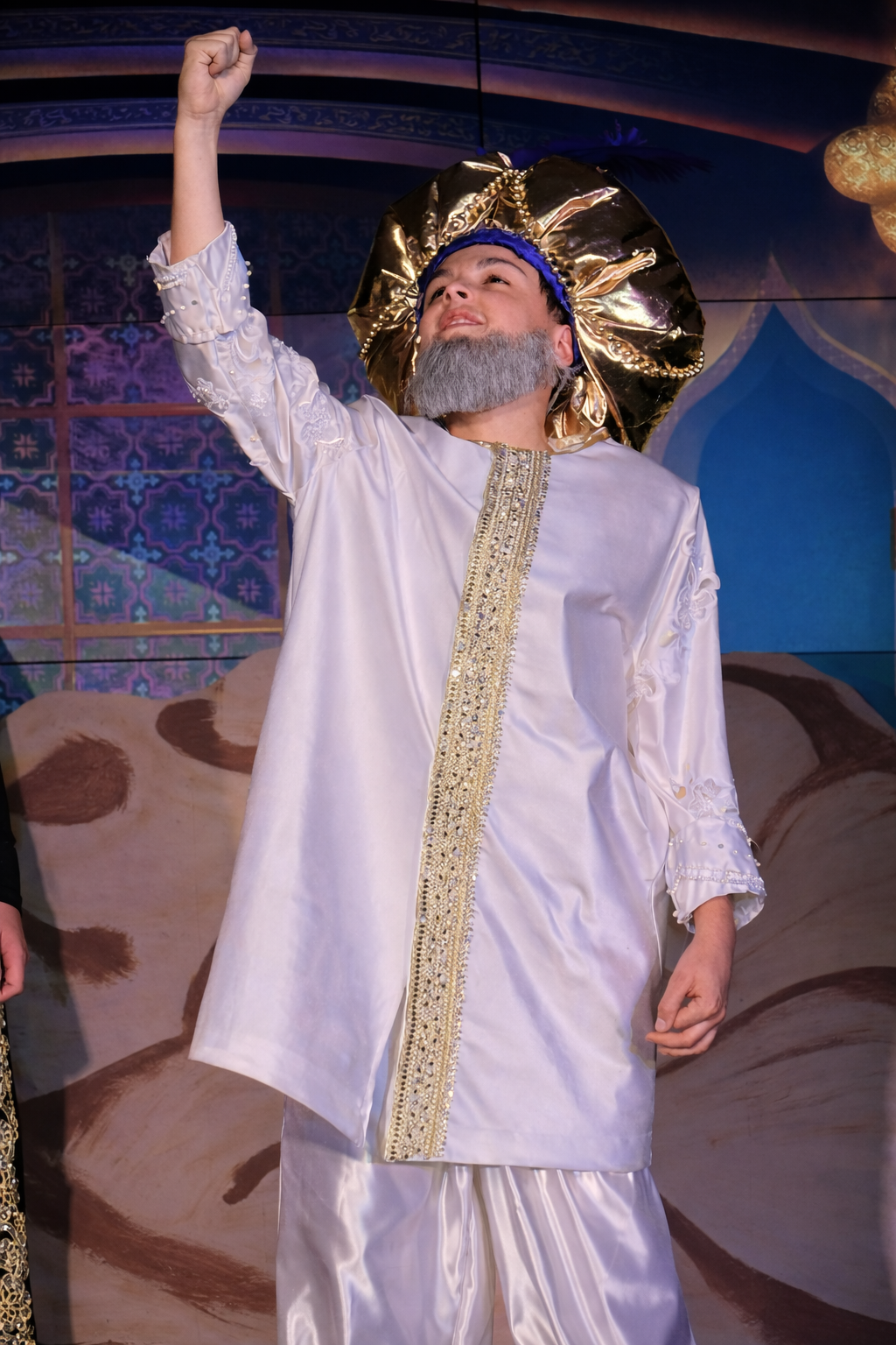 Sultan costume for Aladdin Jr with white tunic, gold trim, and gold turban during a school musical performance scene.