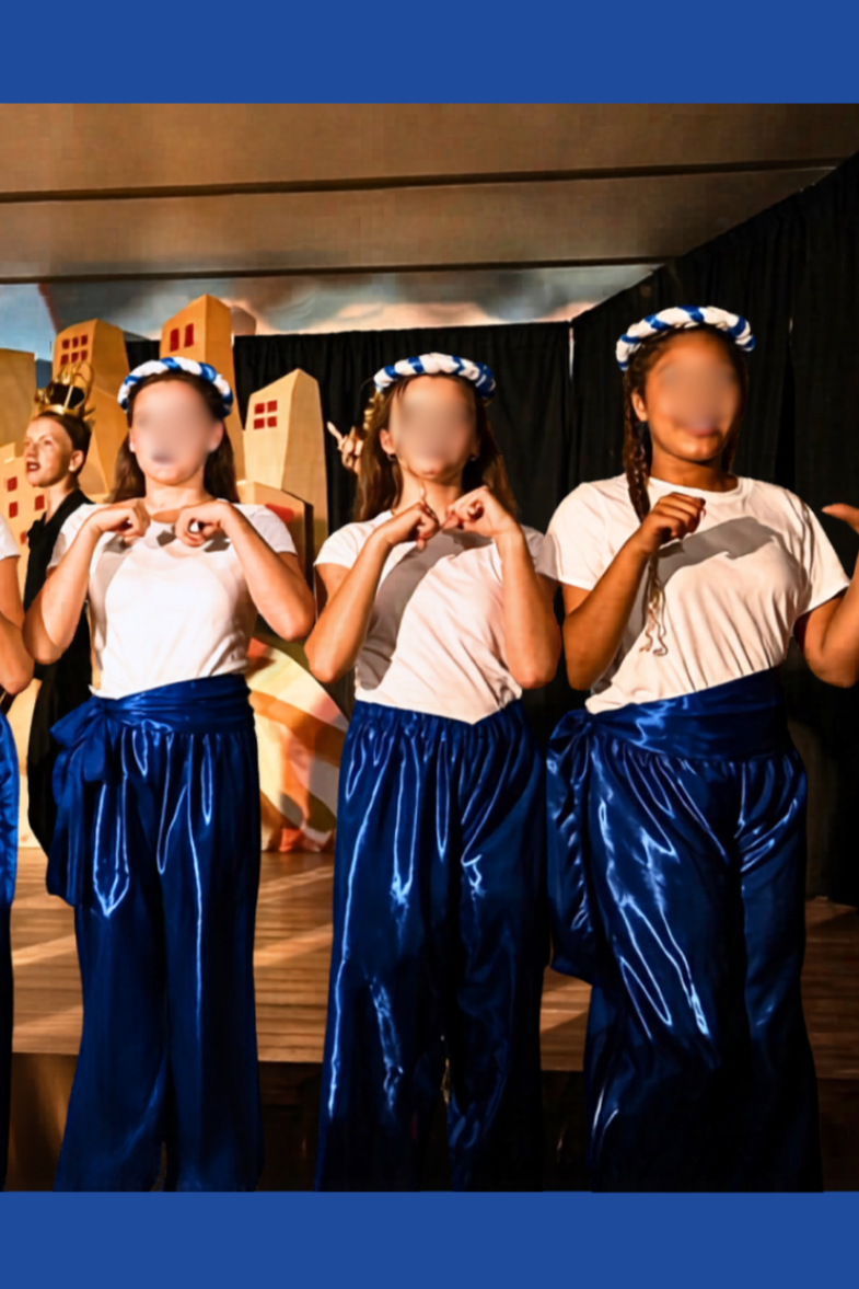 Genie assistants in the Cave of Wonders scene in Aladdin Jr wearing blue satin pants, white tops, and matching braided headbands during a school musical performance.