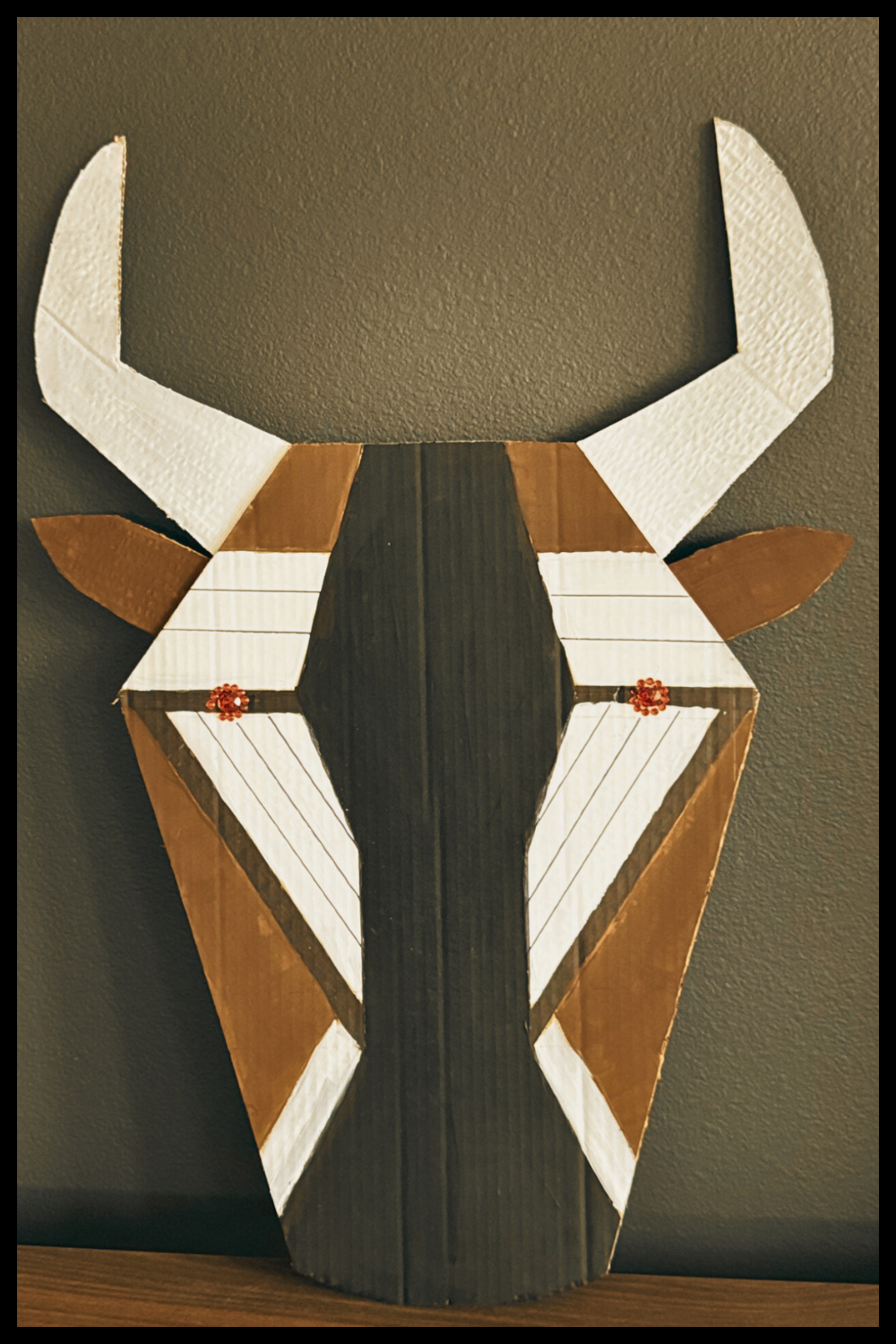 Lion King JR – WIldebeest Geometric Animal Mask: Handmade geometric antelope-inspired mask with angular horns and neutral earth tones for a school theater production.